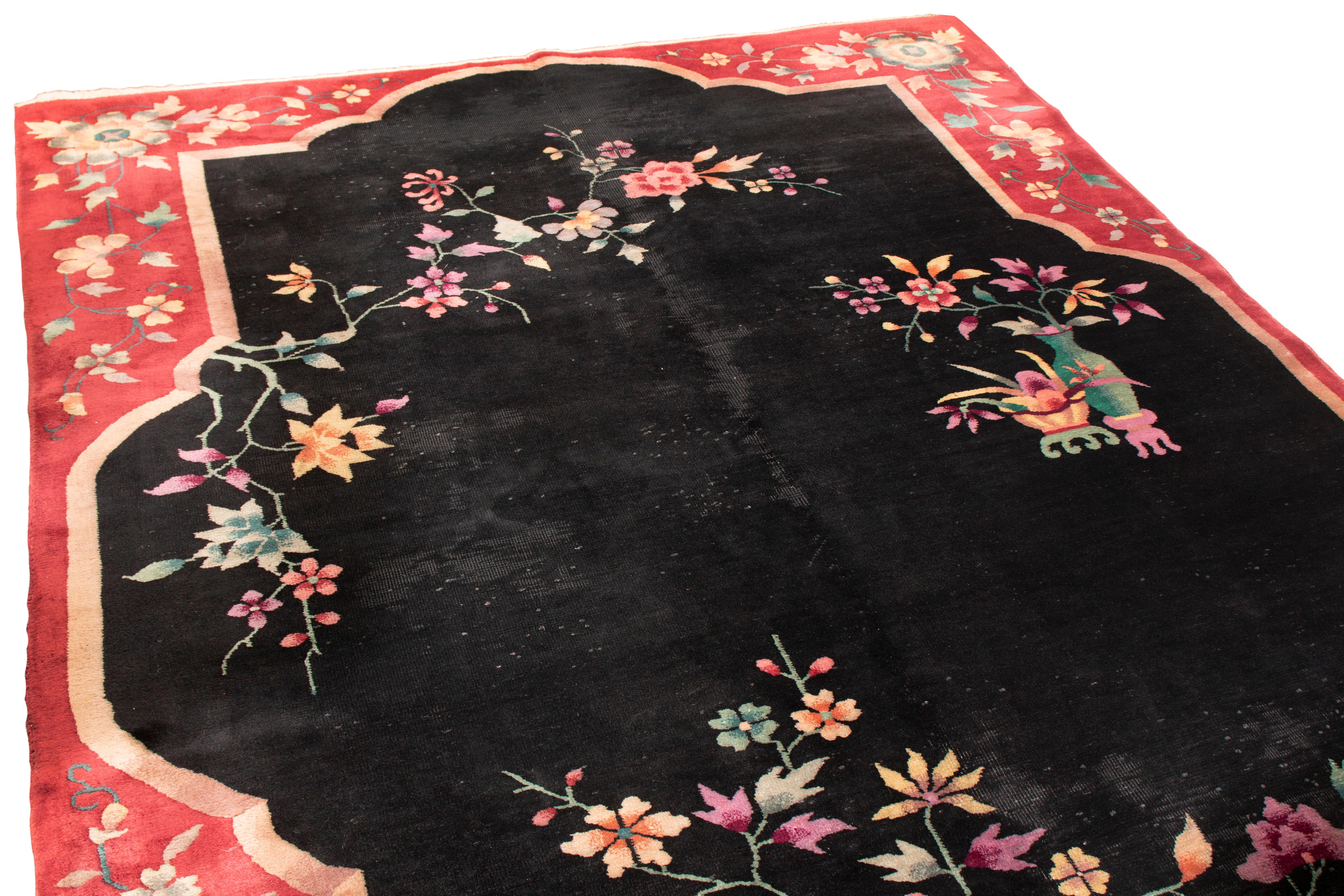 This vintage Chinese wool rug from Rug & Kilim has a traditional style with influences from other vintage families. Originating in China, the hyper-stylized floral patterns, symmetrical in the royal red border but almost one-sided in the black field