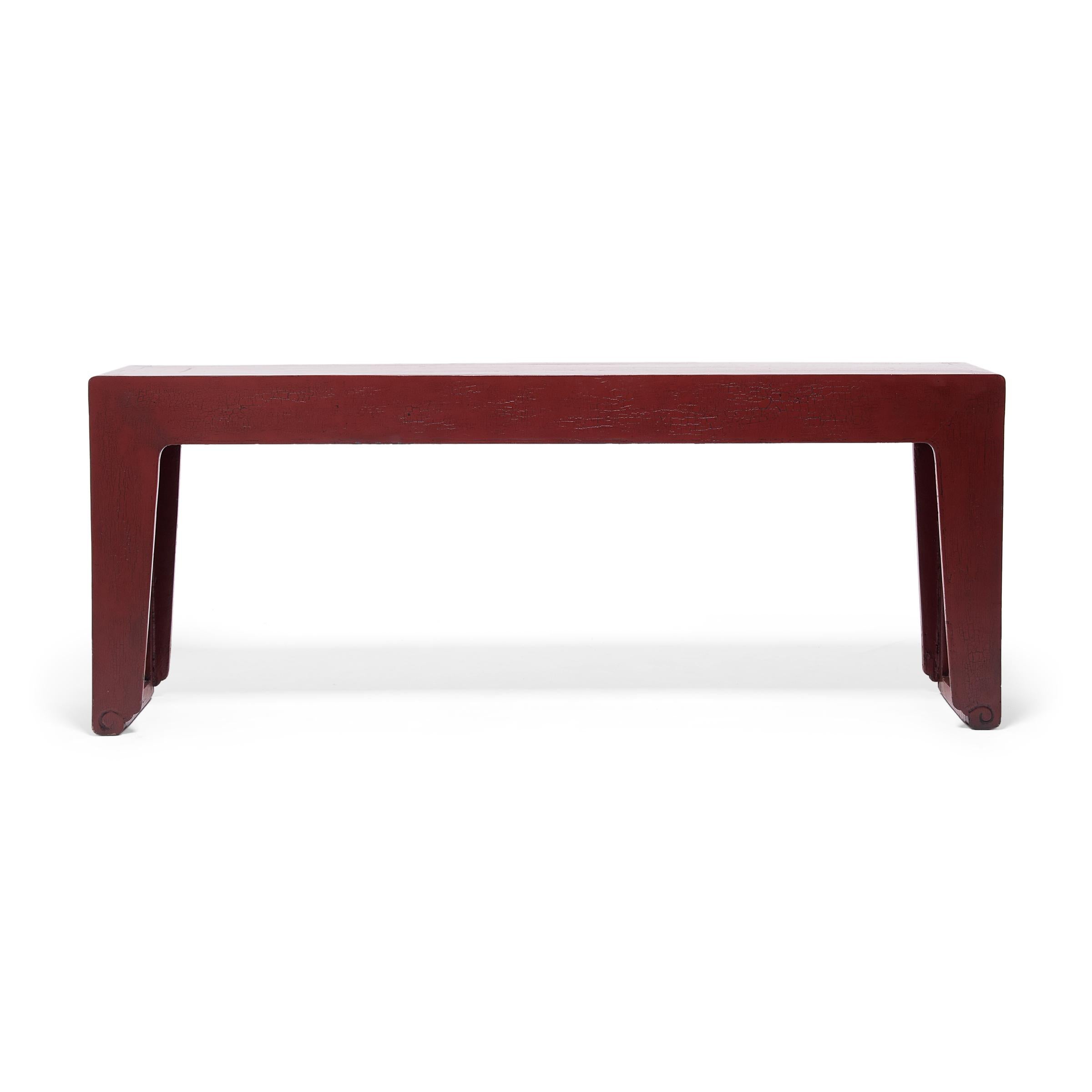 Dated to the early 20th century, this red lacquer console table has a unique waterfall design, the top flowing into the sides as one continuous ribbon. The table is minimally decorated, featuring scrolled feet and a simple apron influenced by the