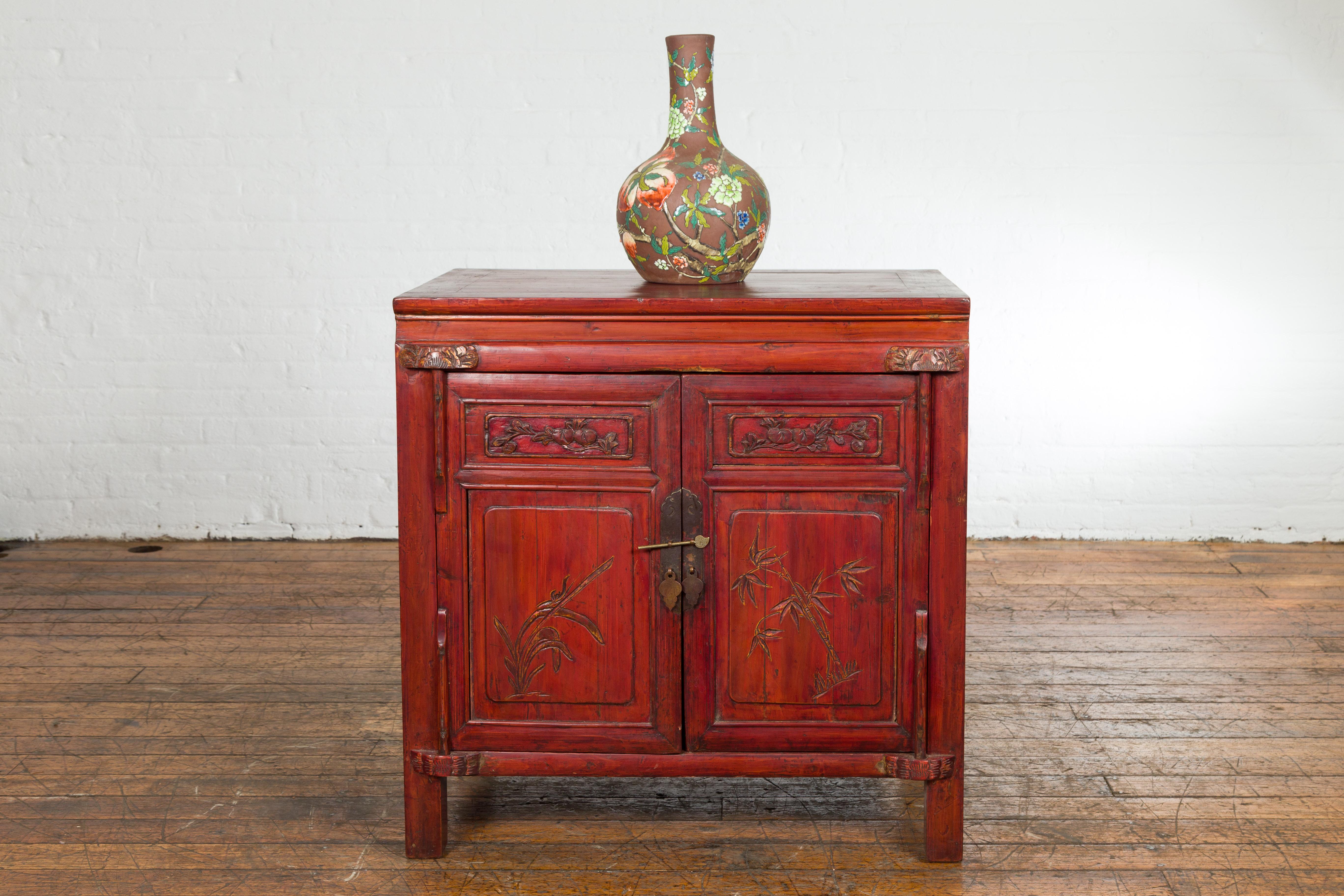 A Chinese late Qing Dynasty period bedside cabinet from the early 20th century, with red lacquer, two doors, hidden drawers, carved décor and brass hardware. Created in China during the late Qing Dynasty period in the early years of the 20th