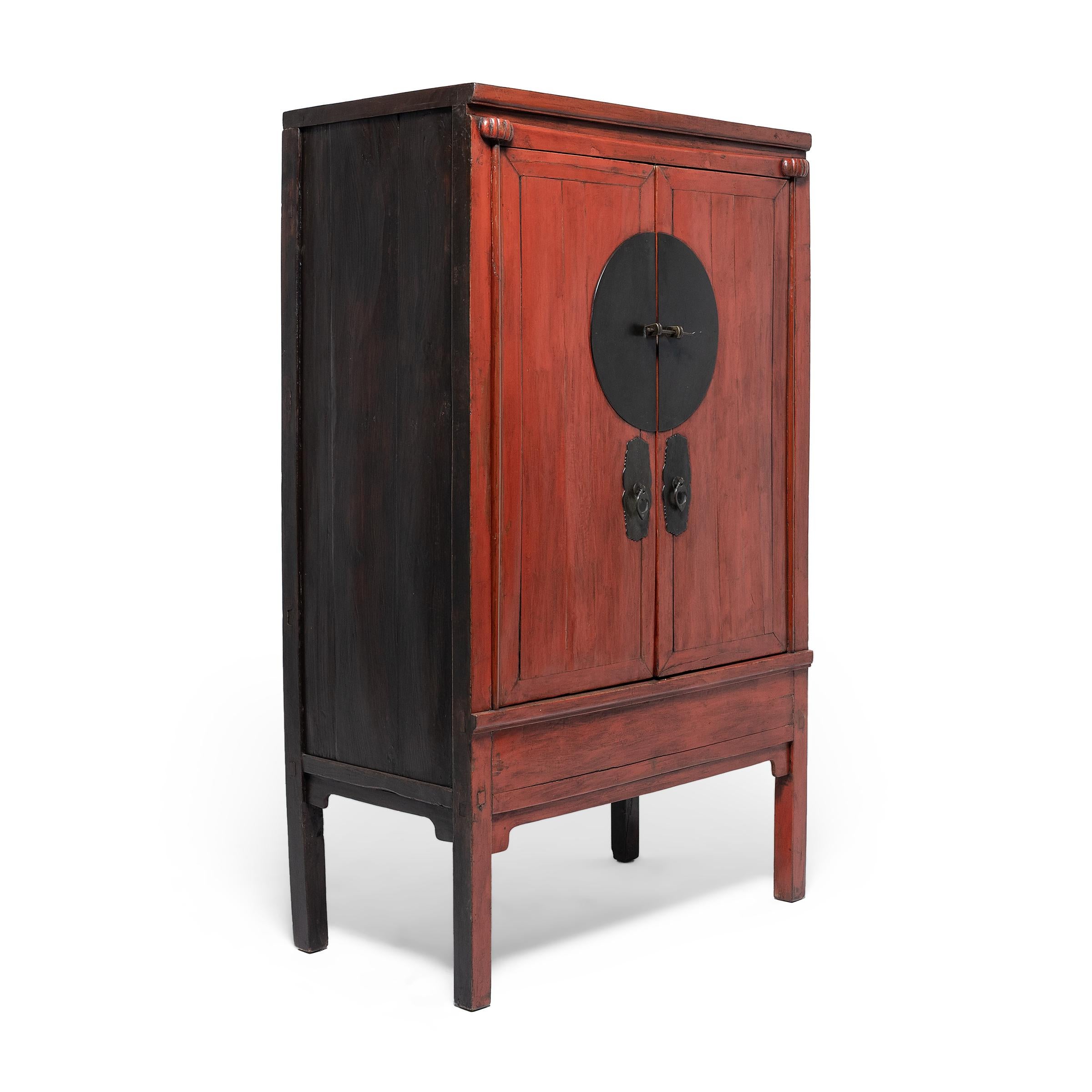Crafted in the late 19th century, this striking red lacquer cabinet was likely part of a traditional wedding dowry, bestowed upon the groom by the bride's family filled with fine silks, linens, and other gifts. The tall cabinet has a clean-lined