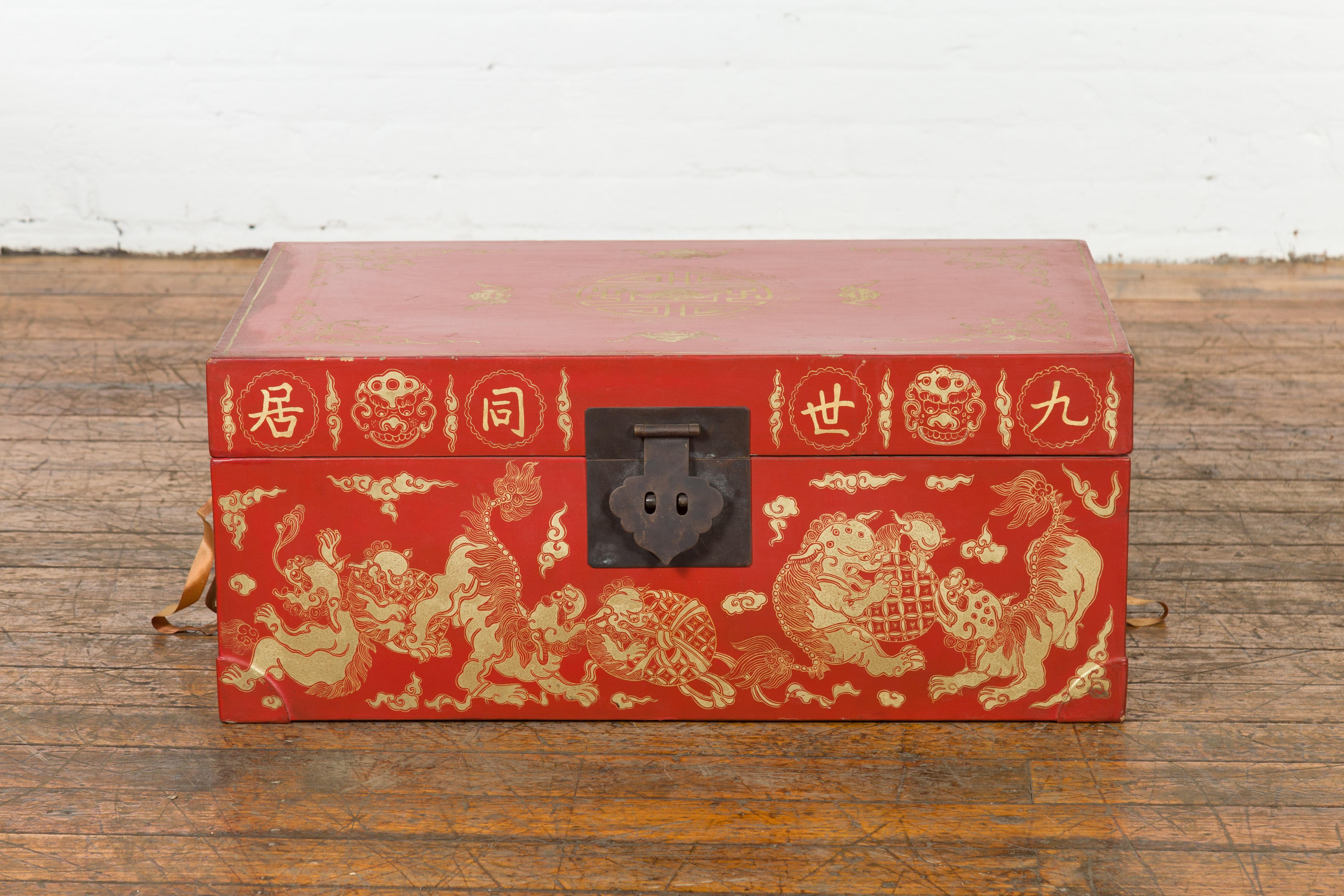 Eine kleine chinesische rot lackierte Hochzeitstruhe aus dem 20. Jahrhundert mit vergoldetem Dekor, das Wächterlöwen, Kalligraphie, Wolken und Fledermäuse darstellt, sowie gelbem Stofffutter und Eisenbeschlägen. Diese im 20. Jahrhundert in China