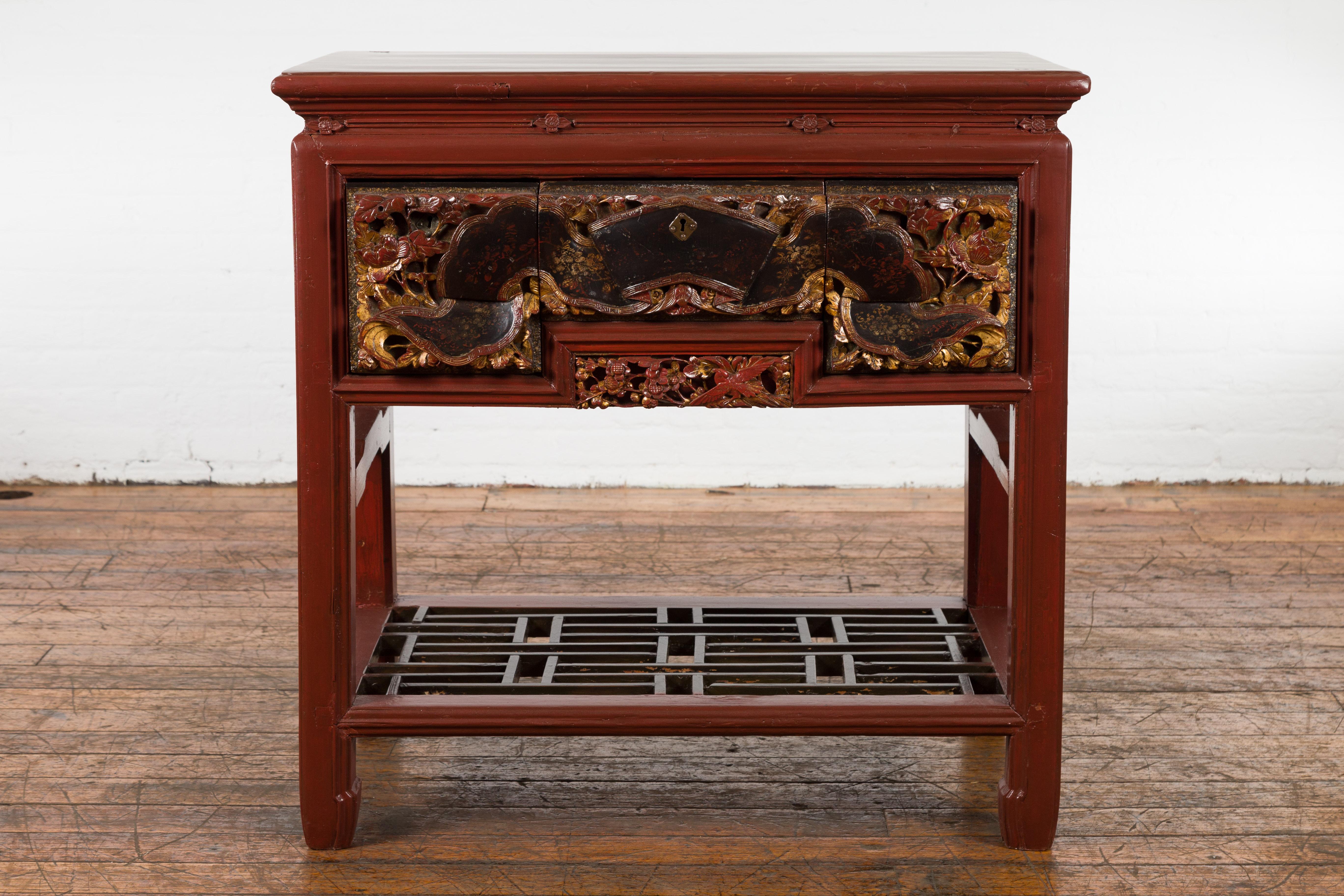 A Chinese red lacquered console table from the 20th century made with 19th century carved pieces, with very unusual hand carved drawers, black and gold highlights and geometric shelf. This exquisite console table features a rectangular top sitting