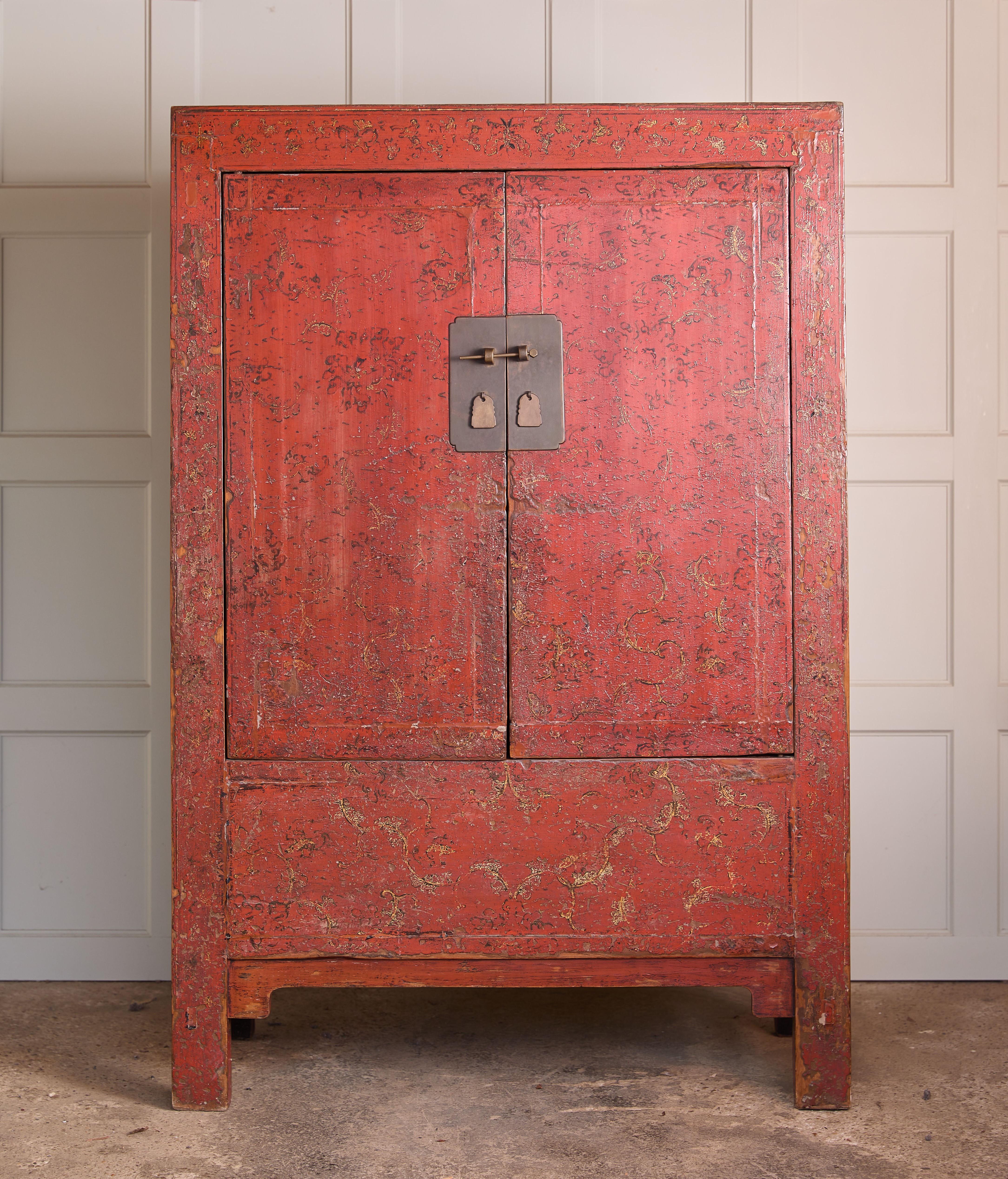 A Chinese red lacquered marriage cabinet, likely from the 18th or 19th century. The doors are decorated with foliate detail, and open to reveal a hanging rail running the whole width. With original brass handles, and finished in traditional red