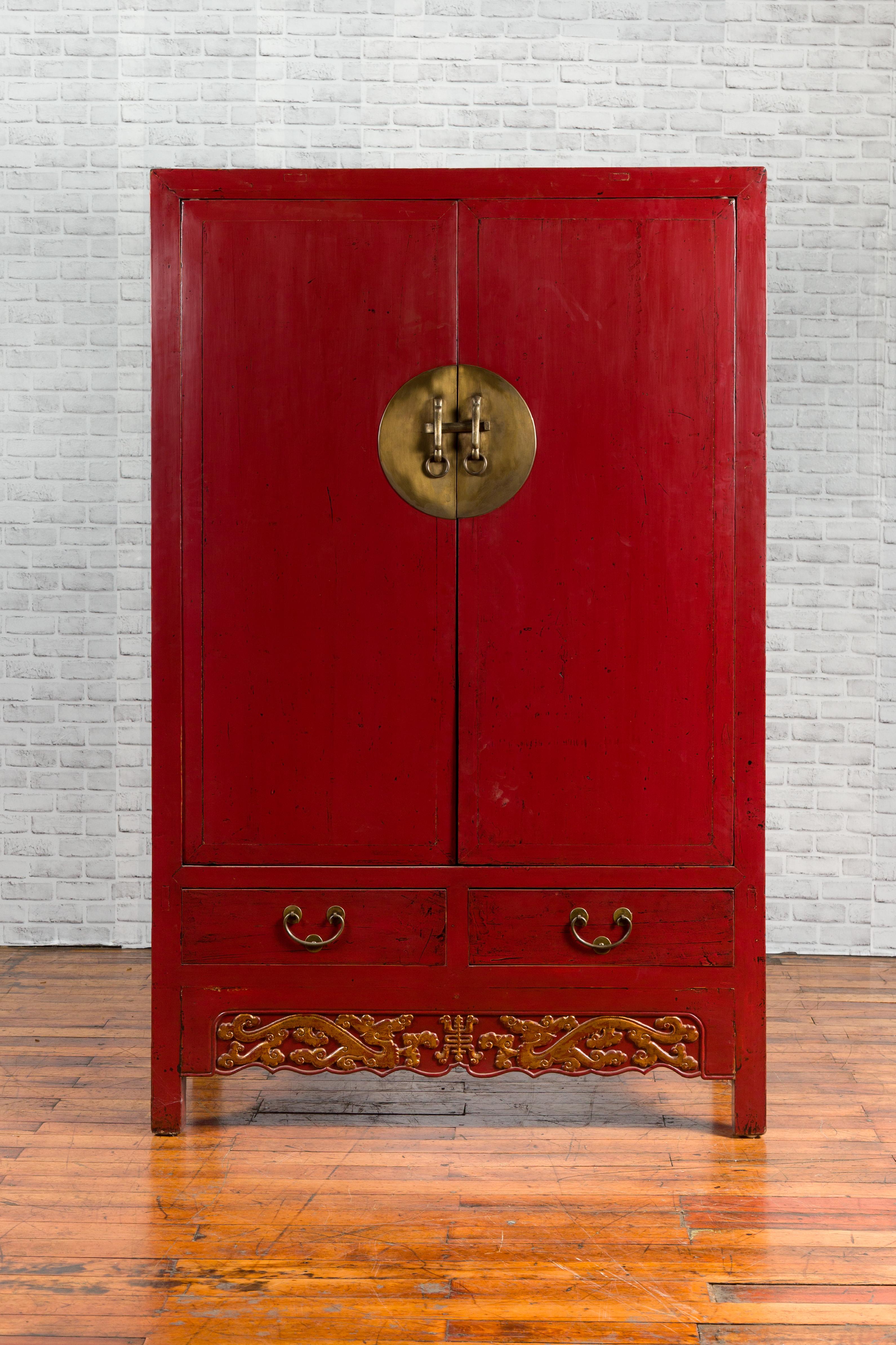 A Chinese red lacquered Qing Dynasty period cabinet from the 19th century, with round brass medallion, drawers and carved gilded apron. Created in China during the Qing Dynasty period, this red lacquered cabinet features two doors fitted with a