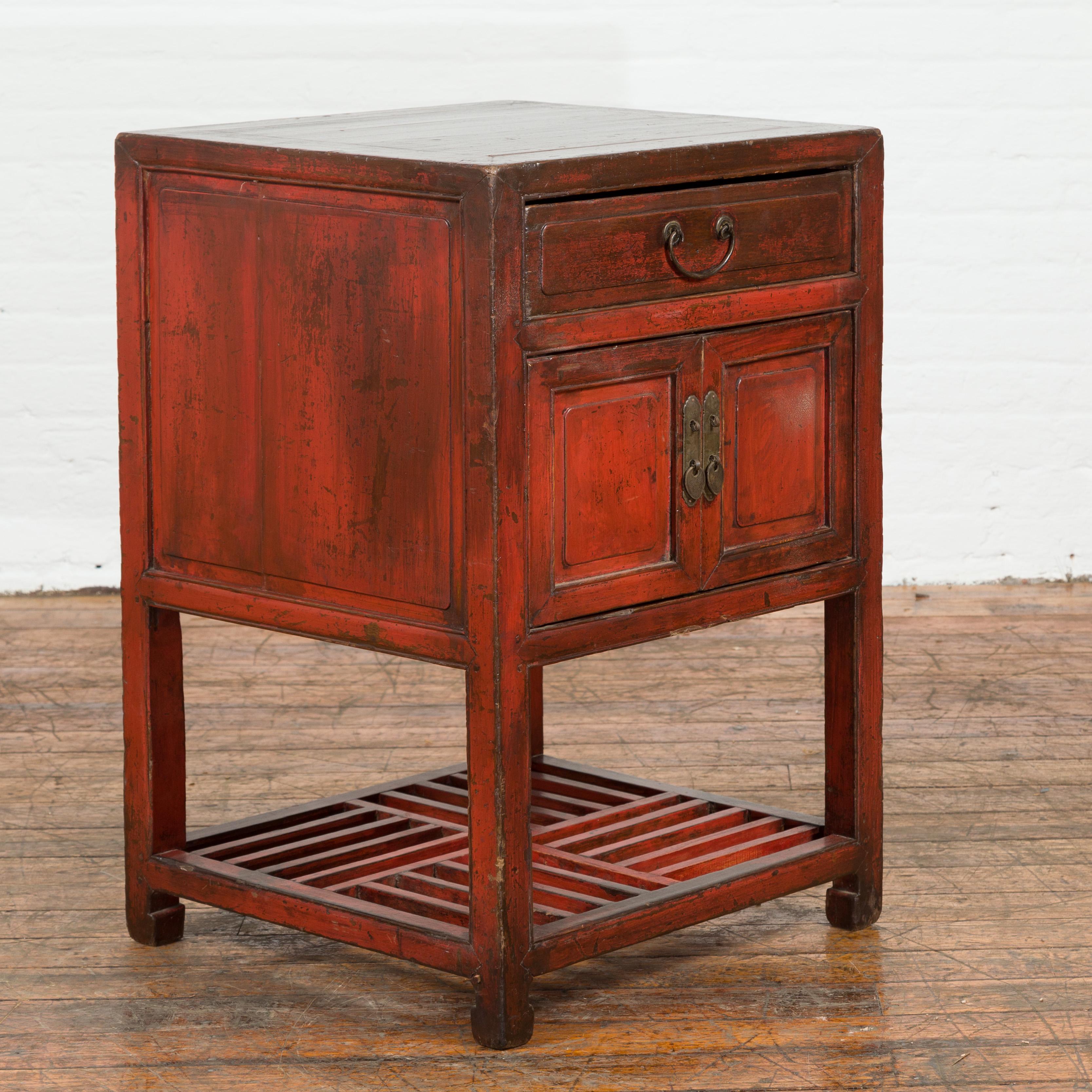 A Chinese Qing Dynasty red lacquer pedestal cabinet from the 19th century with single drawer, double doors and geometric shelf. Created in China during the Qing Dynasty, this small pedestal cabinet features a square top with central board, sitting