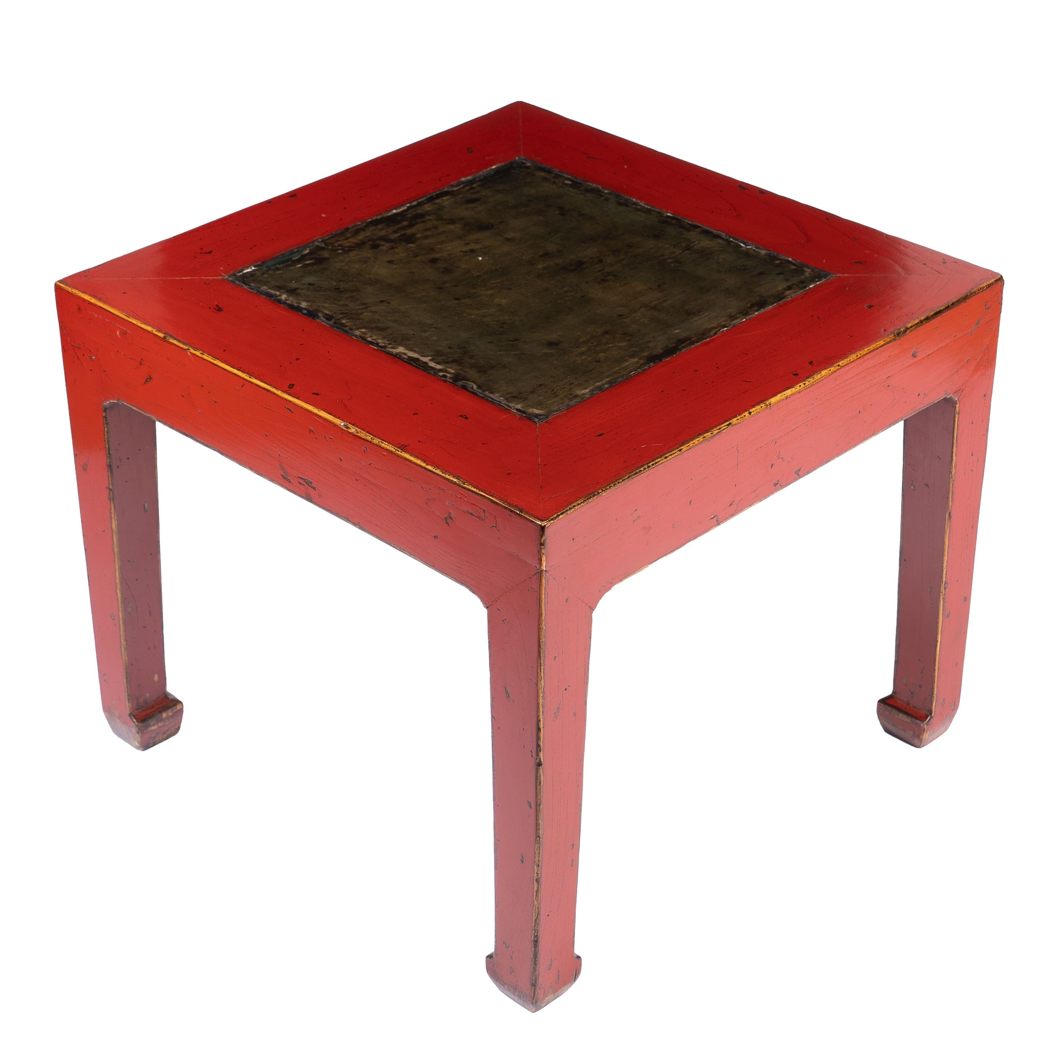 Rot lackierter, quadratischer Tisch mit einer Mittelplatte aus Stein. Die hüftlose Tischplatte wird von vier Vierkantbeinen mit Huffuß getragen. Ausgestattet mit einem früheren Kalligrafiestein.
China, um 1900.