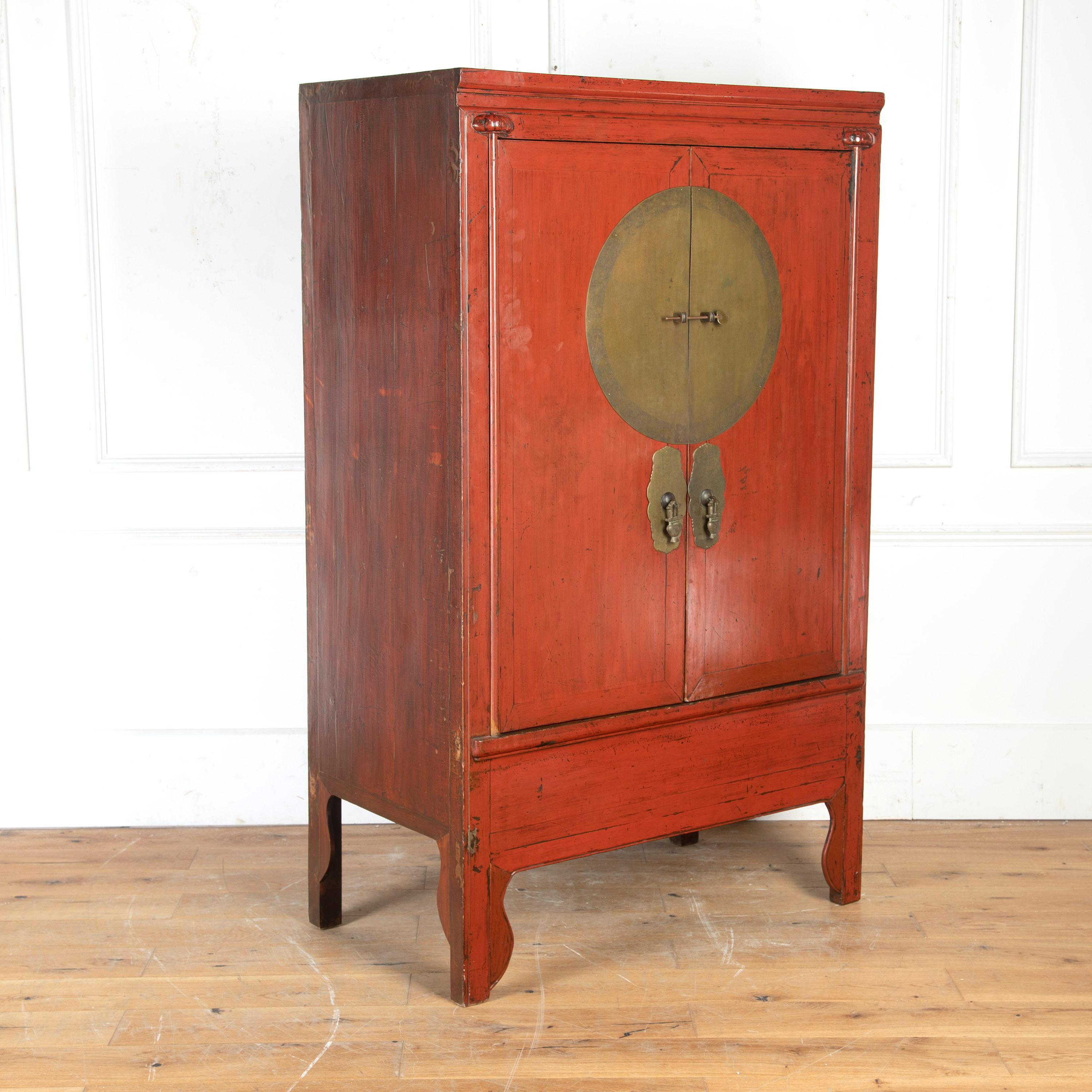 Chinese 19th century red lacquered wedding cabinet, dating from the late period of the Qing Dynasty. 

This wonderful cabinet features two simple doors centred by a large brass medallion and decorative escutcheons. The interior retains its two