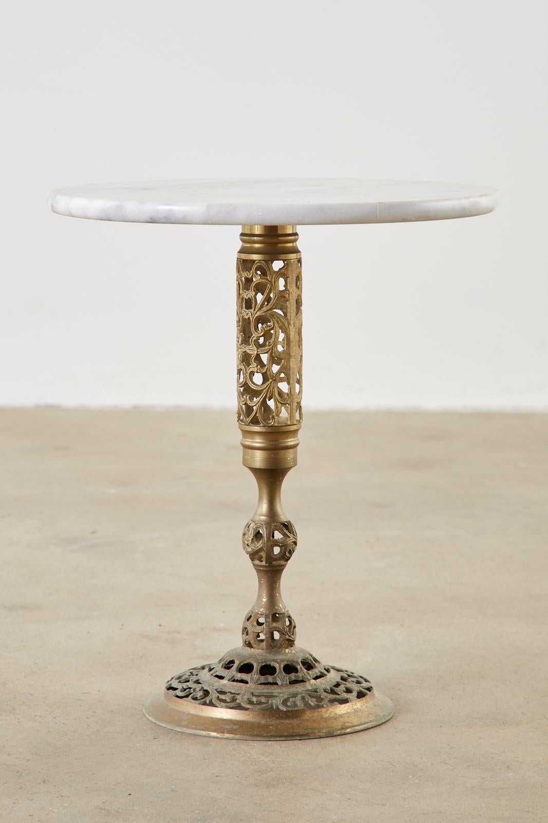Stunning Chinese Hollywood Regency brass drinks table featuring a round Carrara marble top. The pedestal base is decorated with a pierced or reticulated open fretwork pattern with a vine motif. The brass has a beautifully aged, patinated finish.