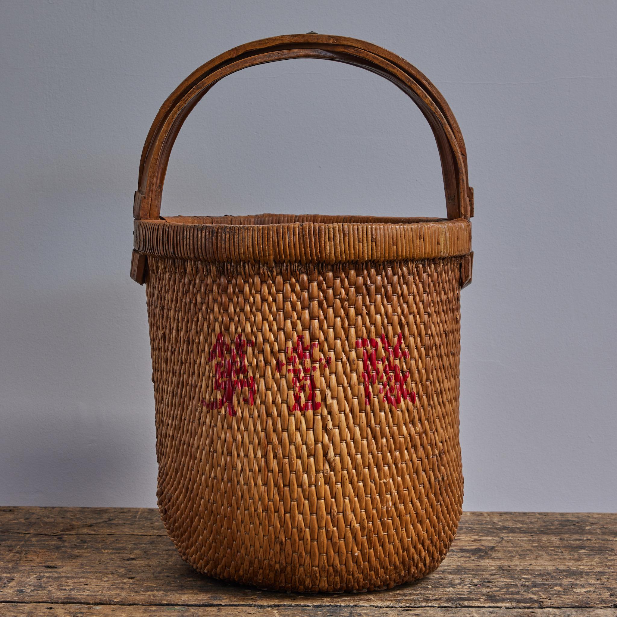 Chinese woven rice basket with simple wooden handle and red painted character decoration. Rustic and pastoral, the fibre is of a deeply toasted hue. Suitable for storage and decorative use alike. 