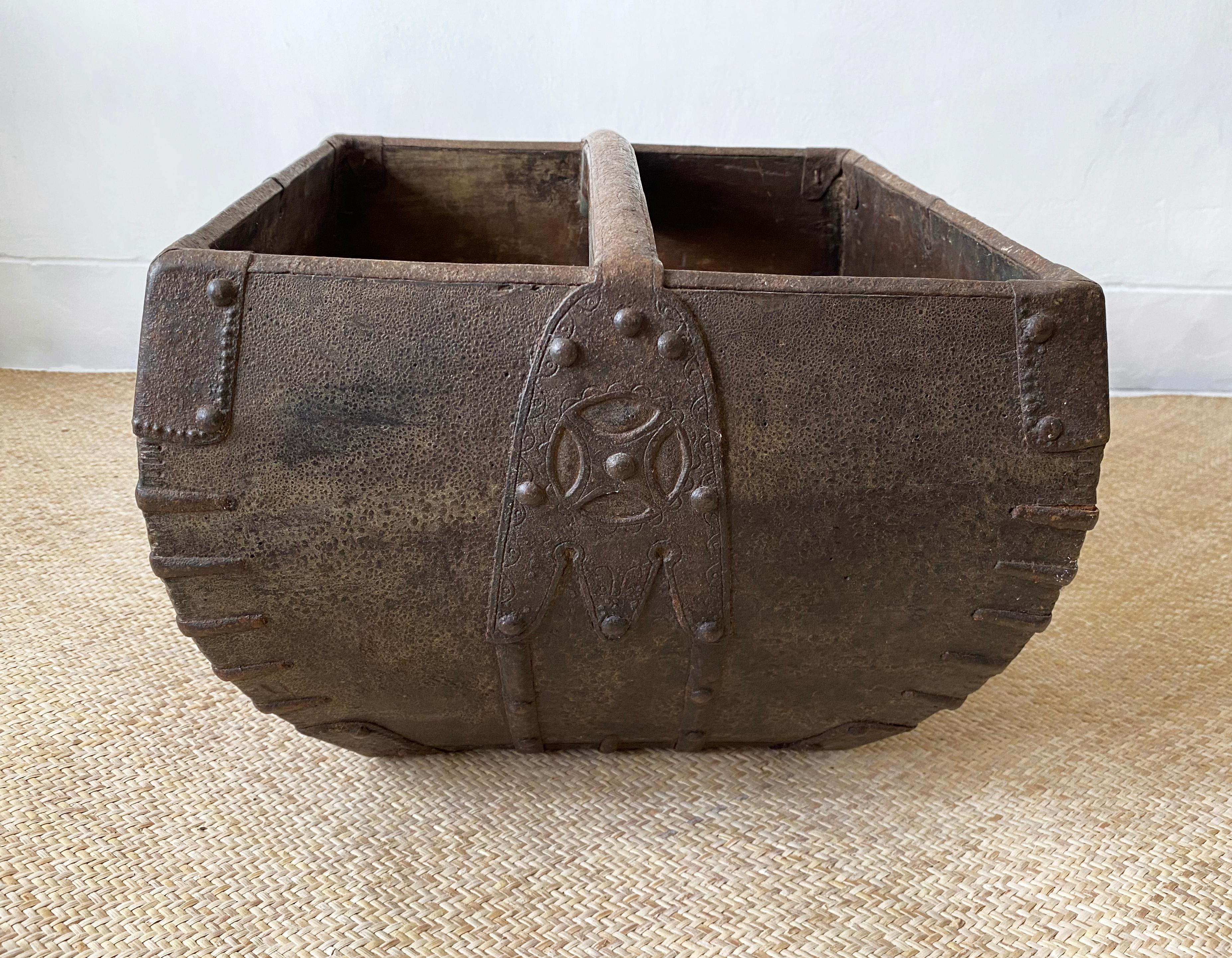 A rice measure container handcrafted more than 100 years from wood and supported by engraved iron edges and an arched handle. There is a wonderful age related patina to the metal and wood. The container is able to hold a Dou of rice a once abundant
