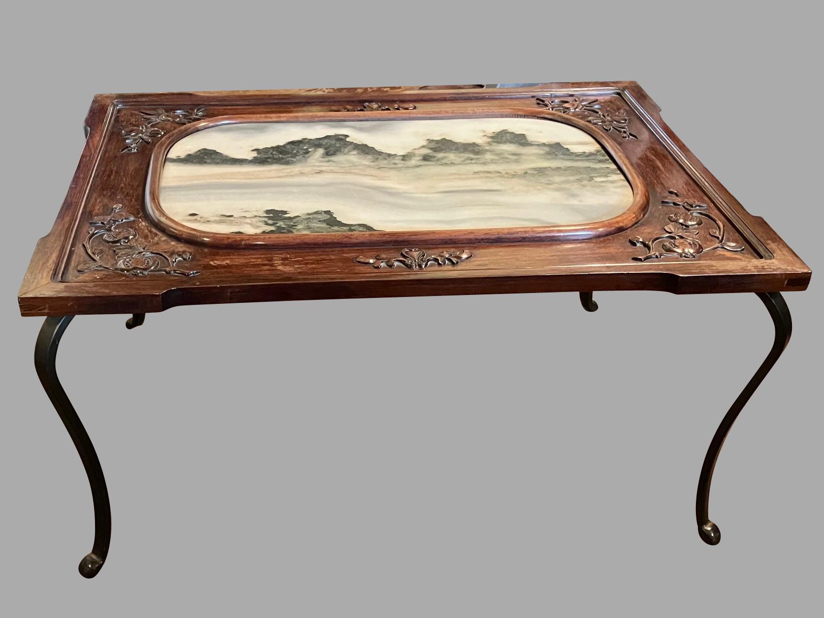 A beautiful custom made Chinese low table, the hardwood top with a central marble inset depicting a stylized pastoral mountain landscape, supported by steel cabriole legs. The marble center is surrounded by a lovely foliate carved hardwood frame