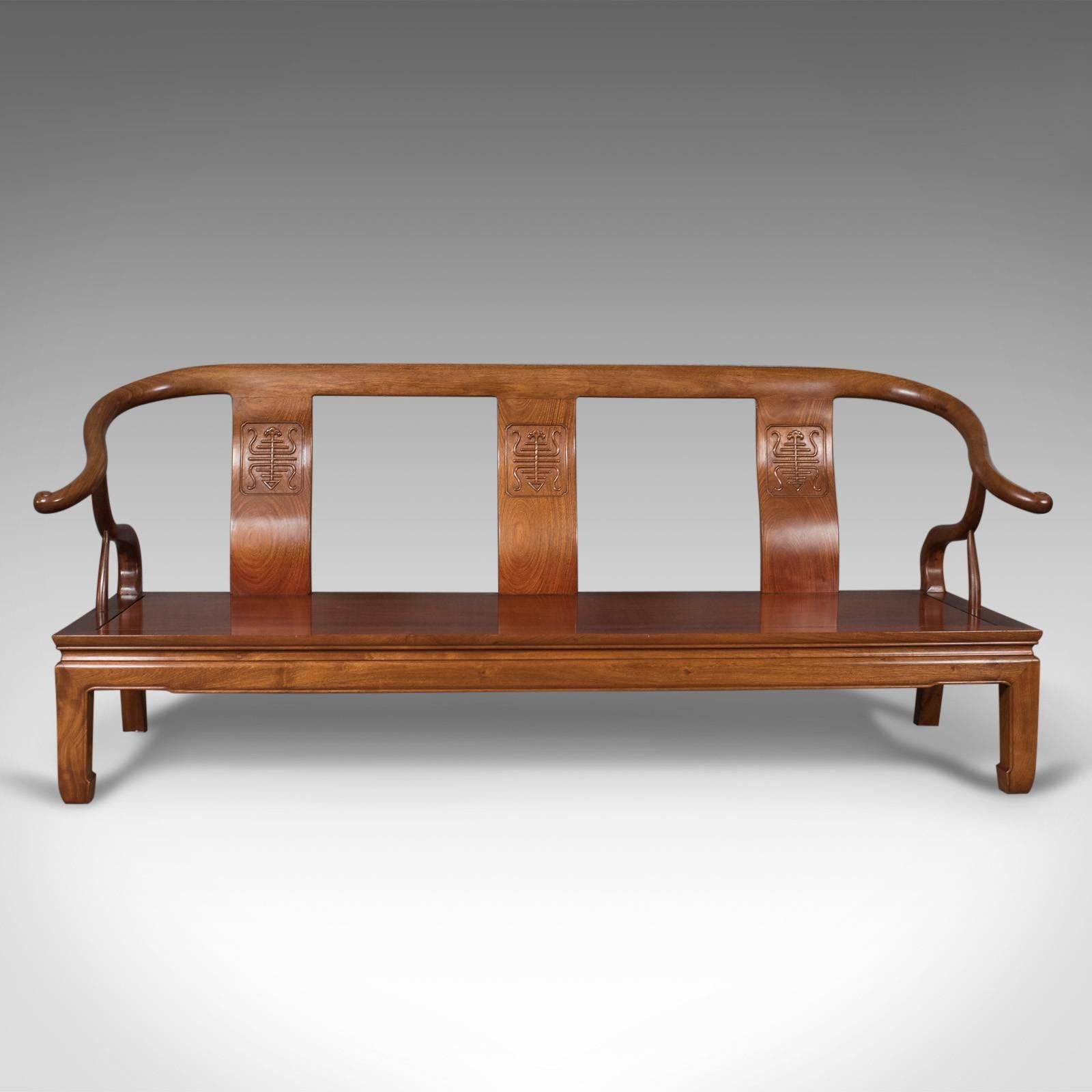 This is a Chinese rosewood three-seat bench in traditional form, dating to the late 20th century.

In super condition with good consistent color
Shaped crest rail runs sinuously into 'cow horn' arms
Oblique scrolled terminals to the
