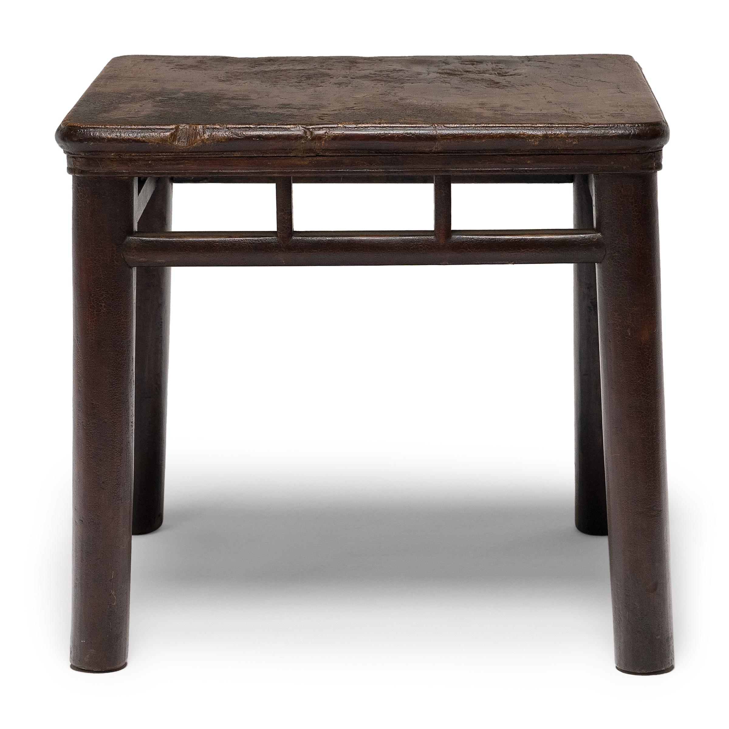 This square side table dates to the mid-19th century, crafted of elmwood (yumu) using mortise-and-tenon joinery with thick, round legs and an overhung, solid plank top. Found at the center of social activity, Chinese square tables such as this were
