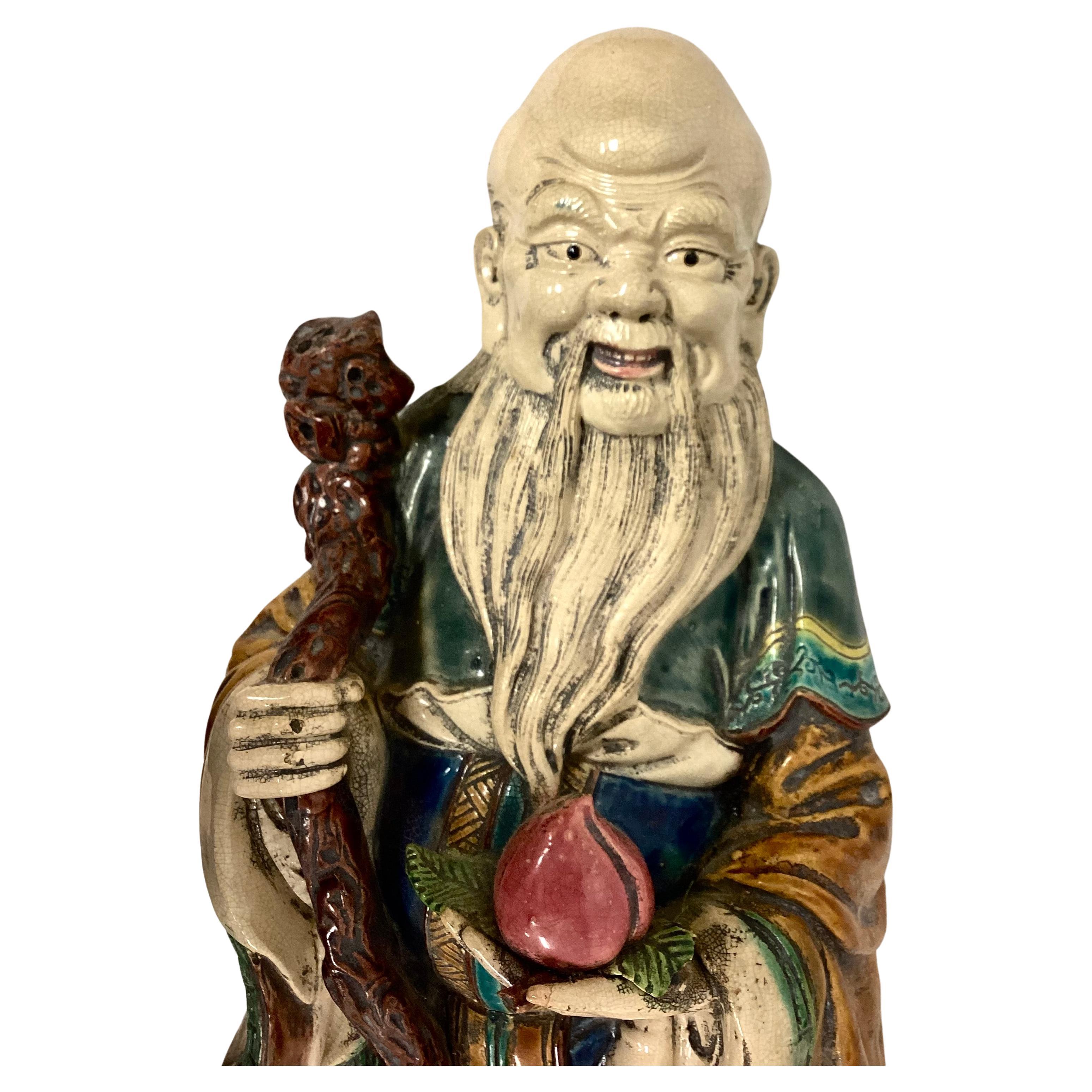 Große chinesische Sage aus dem 19. Jahrhundert aus schwerem Porzellan. Mann in traditionellem Gewand, der in der einen Hand einen großen Spazierstock und in der anderen eine Lotusblume hält. Mit tollen Farben wie Rosa, Blau, Grün, Braun und