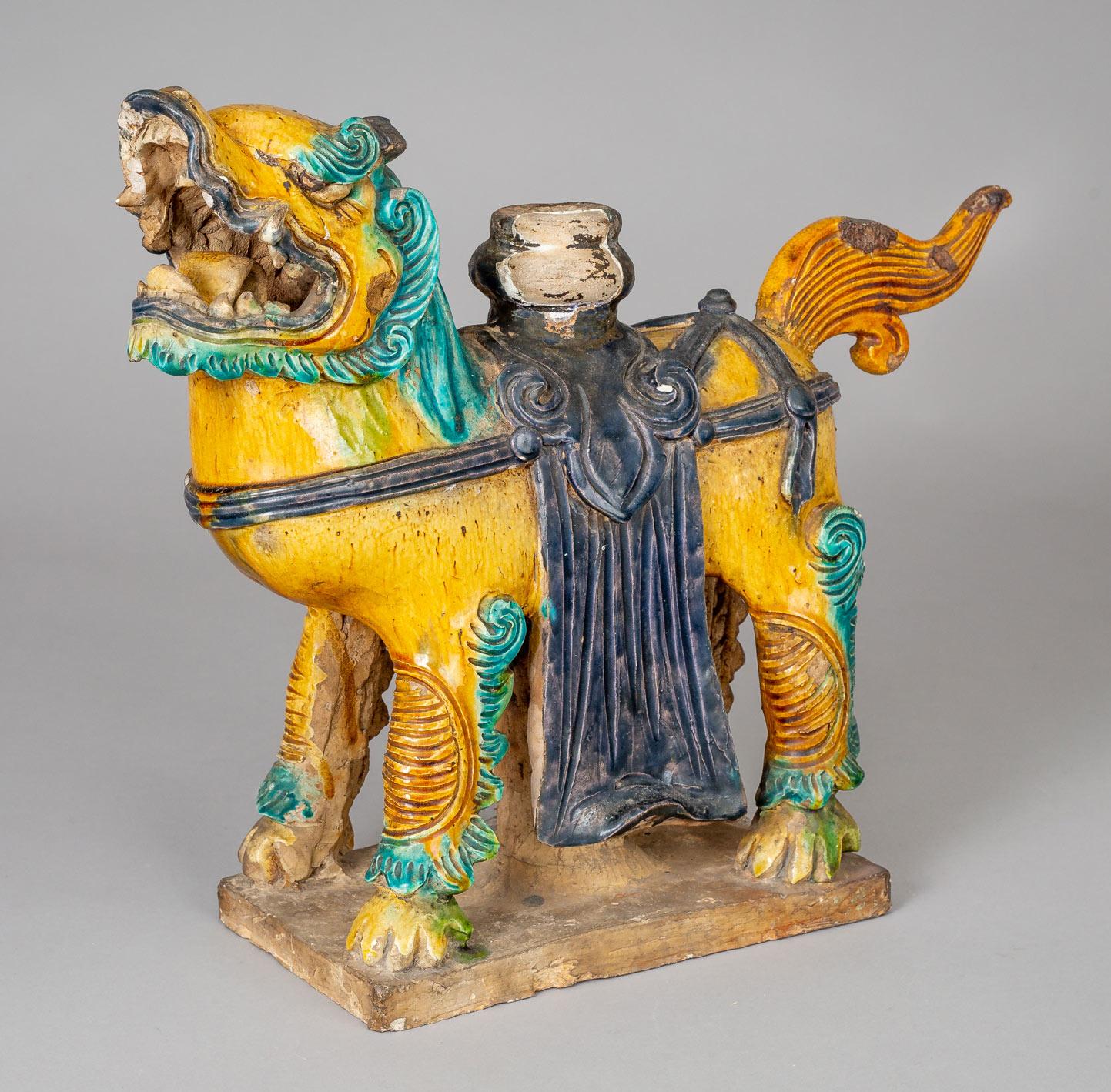 Large and antique Chinese Sancai glazed pottery guardian lion, its mouth drawn back in a snarl, wearing a shawl and carrying an urn on its back, standing four square on a plinth. Possibly a roof ridge tile. Provenance: The Sears Estate.