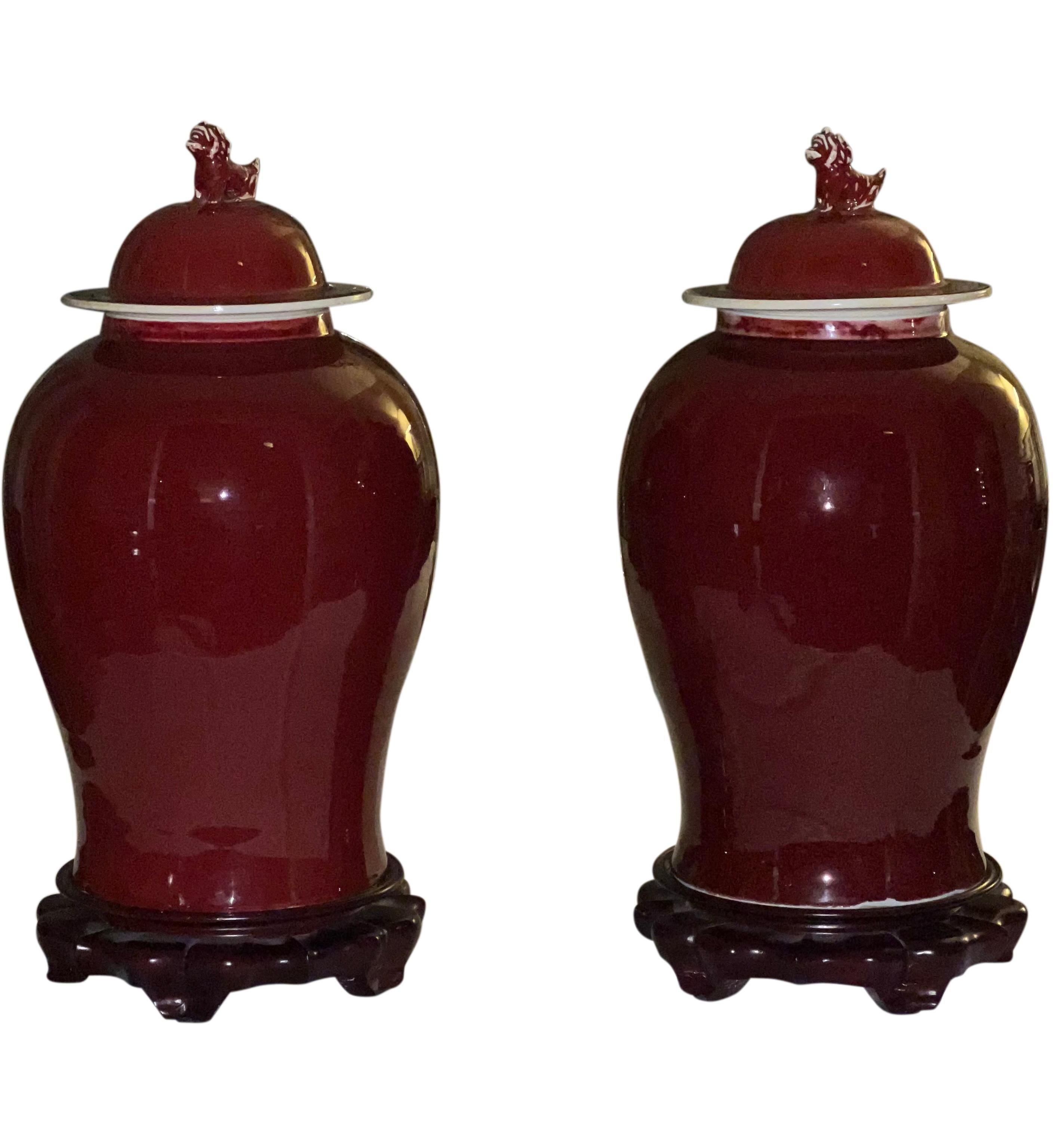 Beautiful pair of Chinese Sang de Boeuf glazed ginger jars on rosewood stands. The jars feature protective Chinese guardian lions, known as foo dogs in the West, on the tops of the lids. A deep Sang de Boeuf (oxblood) glaze give the jars gorgeous