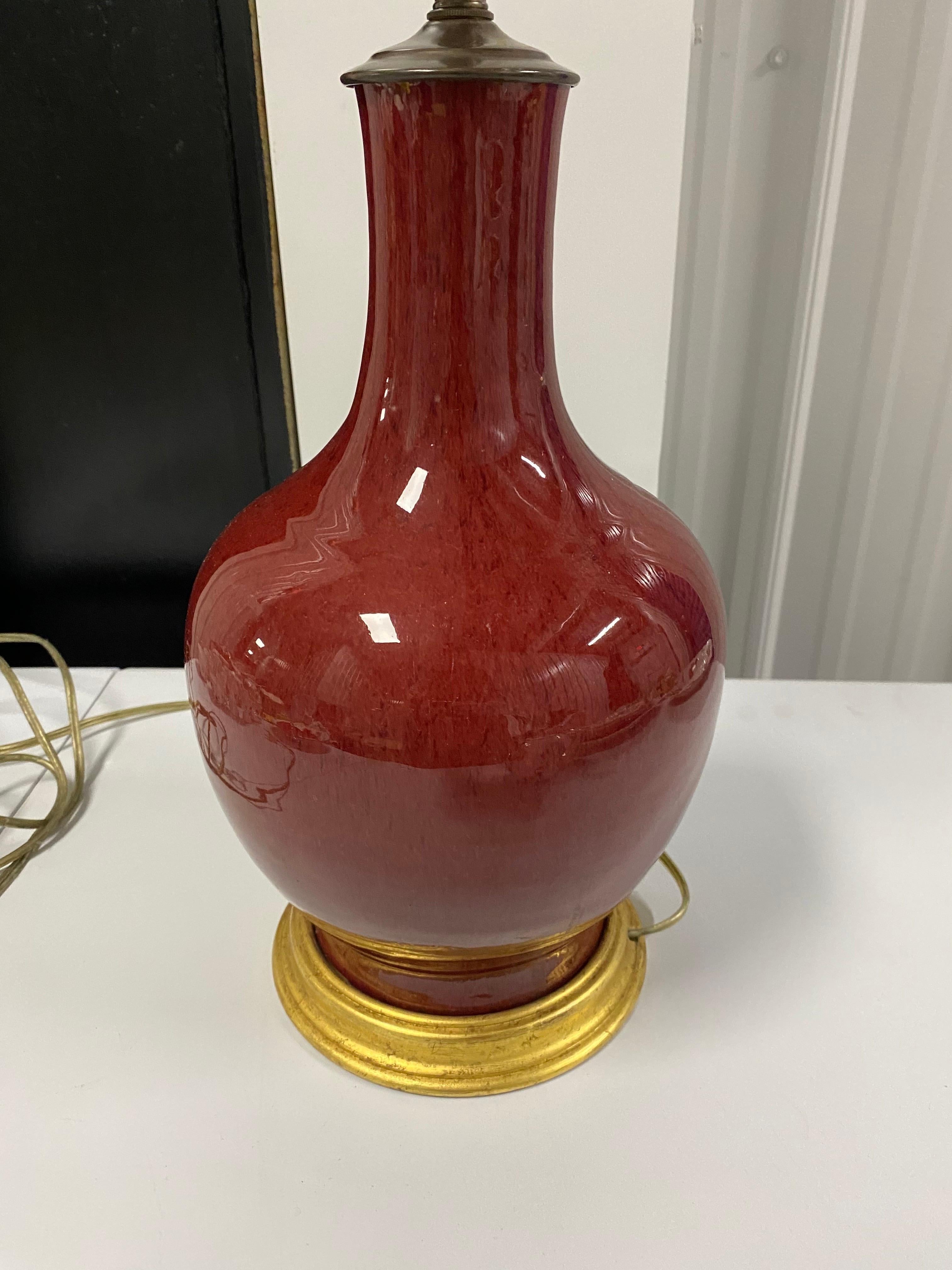 One Chinese Sang-de-Boeuf glazed red vase, c. 19th century, made into a lamp. Round bulbous gourd form with an elegant clean neck glazed in deep red glaze. The vase is antique with a later gilded wooden base and lighting components added. Also