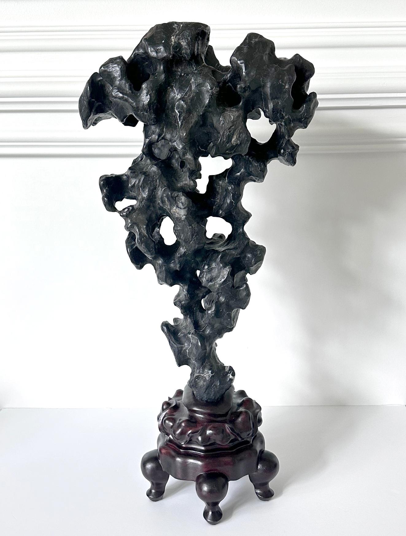 Le rocher élancé du savant Taihu, de forme A, est présenté sur un support en bois sculpté sur mesure. Merveilleuse forme bien équilibrée, la roche présente une image proche du mirage entre l'avant et l'arrière. Obsidienne noire presque pure avec des
