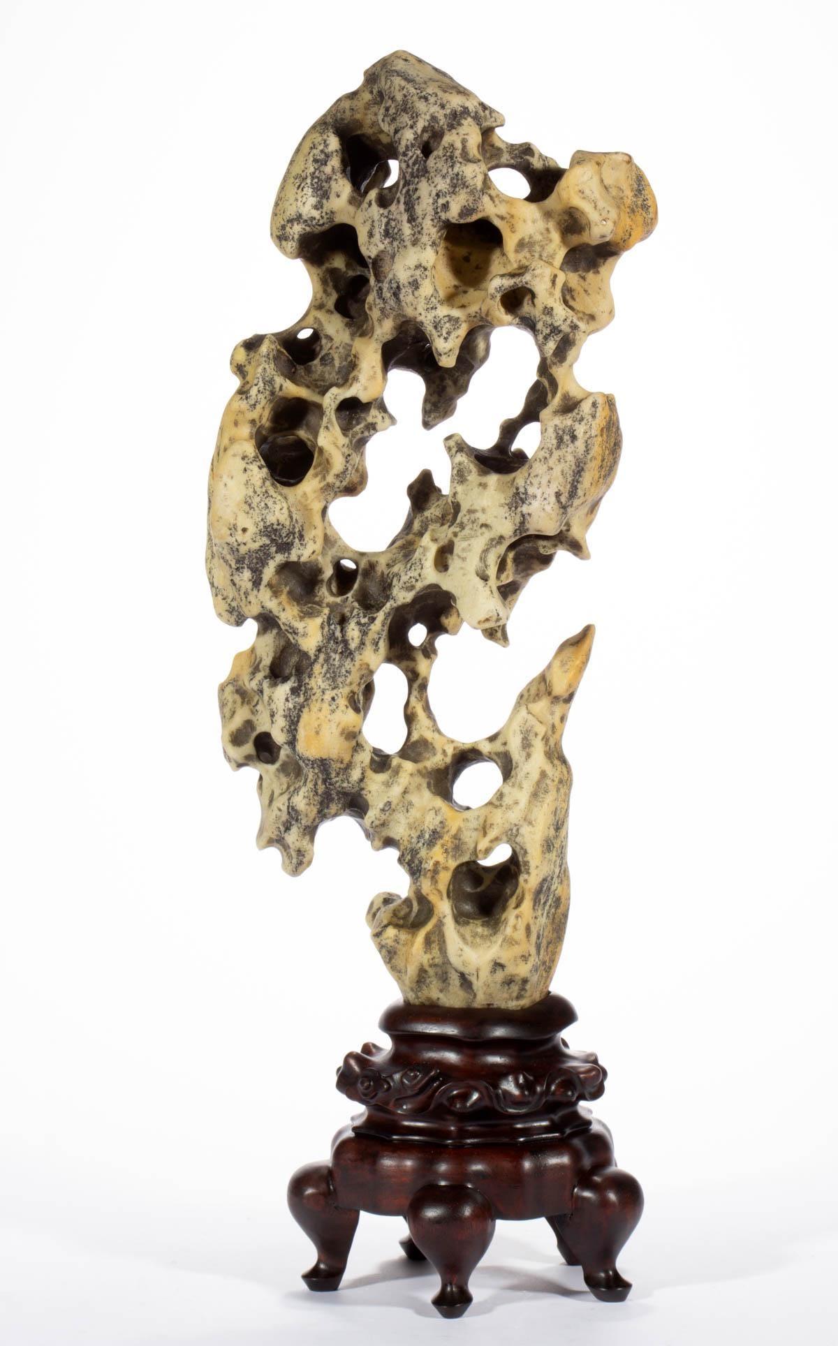 This is a slender Taihu scholar rock in an upright form displayed on a custom wood stand. Wonderful and well-balanced form, the rock has a nearly mirage image between the front and the back. It is of an uncommon waxy yellow color with black deposits