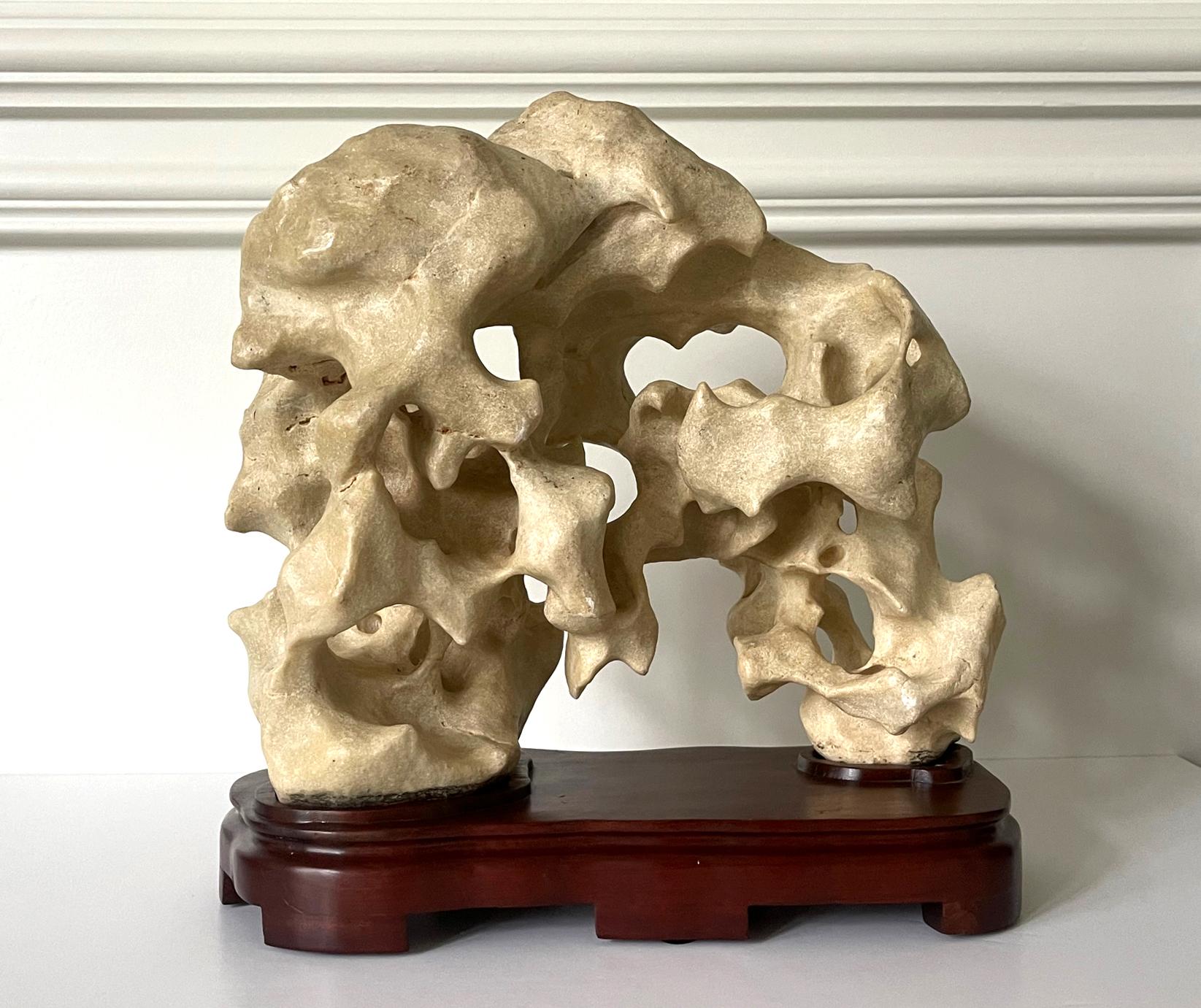 A Taihu scholar rock in a horizonal bridged form balanced on a custom wood stand. The stone, in a nearly pure soft white color, display a well-weathered surface with some patina. The surface features various natural geological characters and