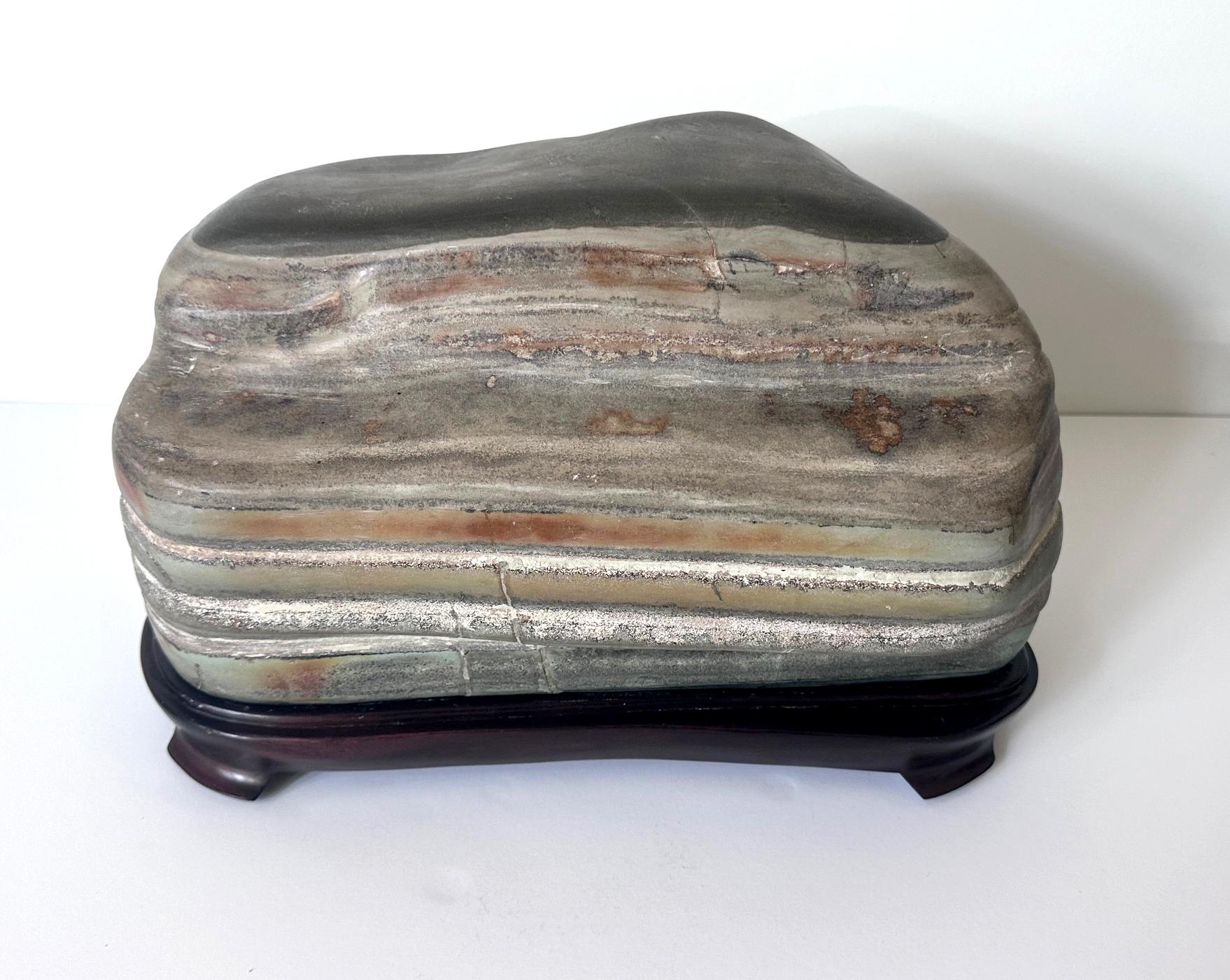 Une pierre de lettré chinoise de type CIRCA présentée sur un support en bois confirmé sculpté, vers les années 1990. Le Caitao, qui signifie poterie colorée en chinois, est un type de pierre savante nouvellement découvert en 1993. Depuis, il a gagné