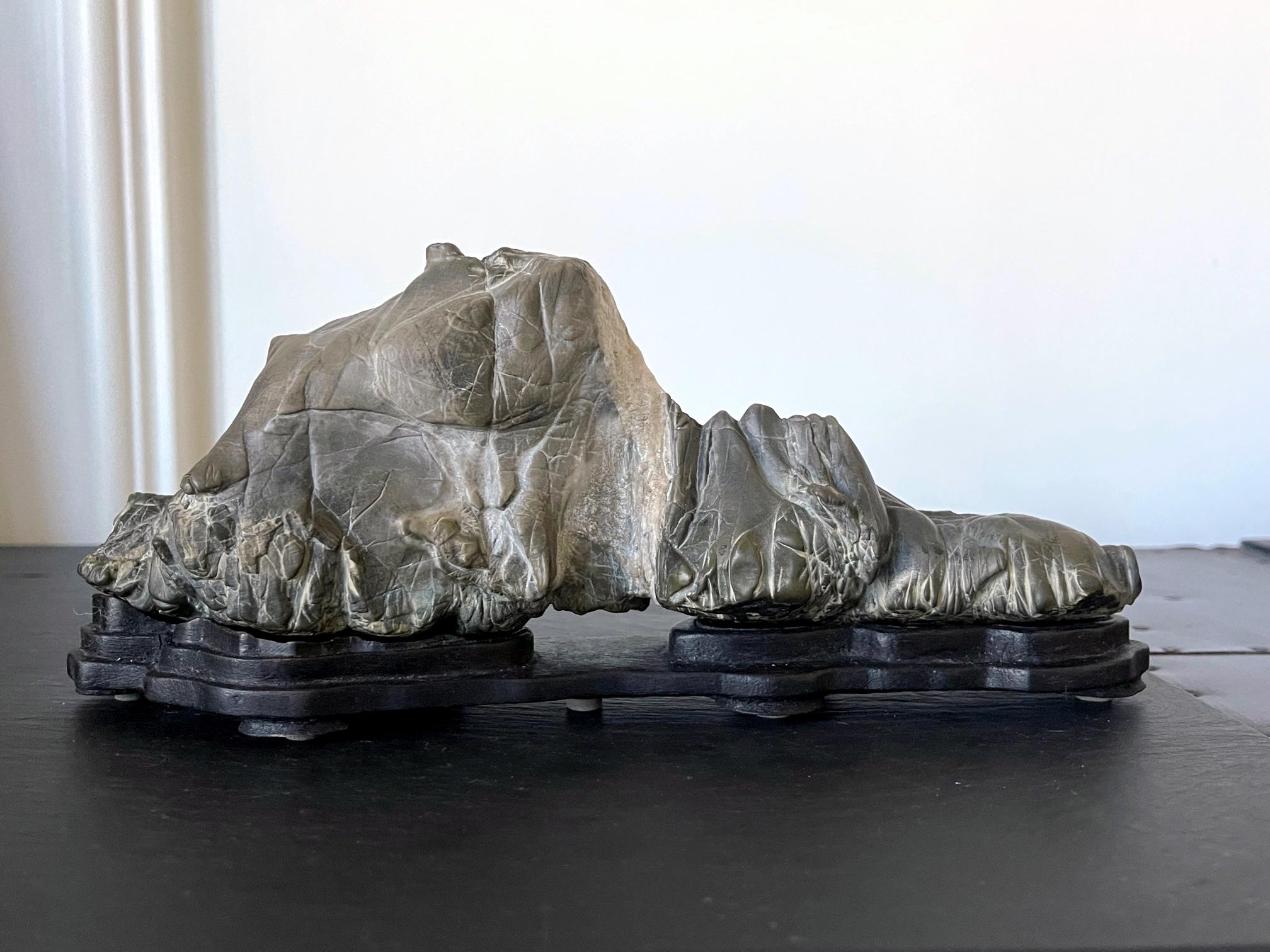 A small desk top Chinese scholar stones (also known as Gong Shi, meditation stone and spirit rock) on a fitted display wood stand circa 19th century. This is likely a grey Lingbi type stone with subtle arch mimics a horizontal mountain range. The