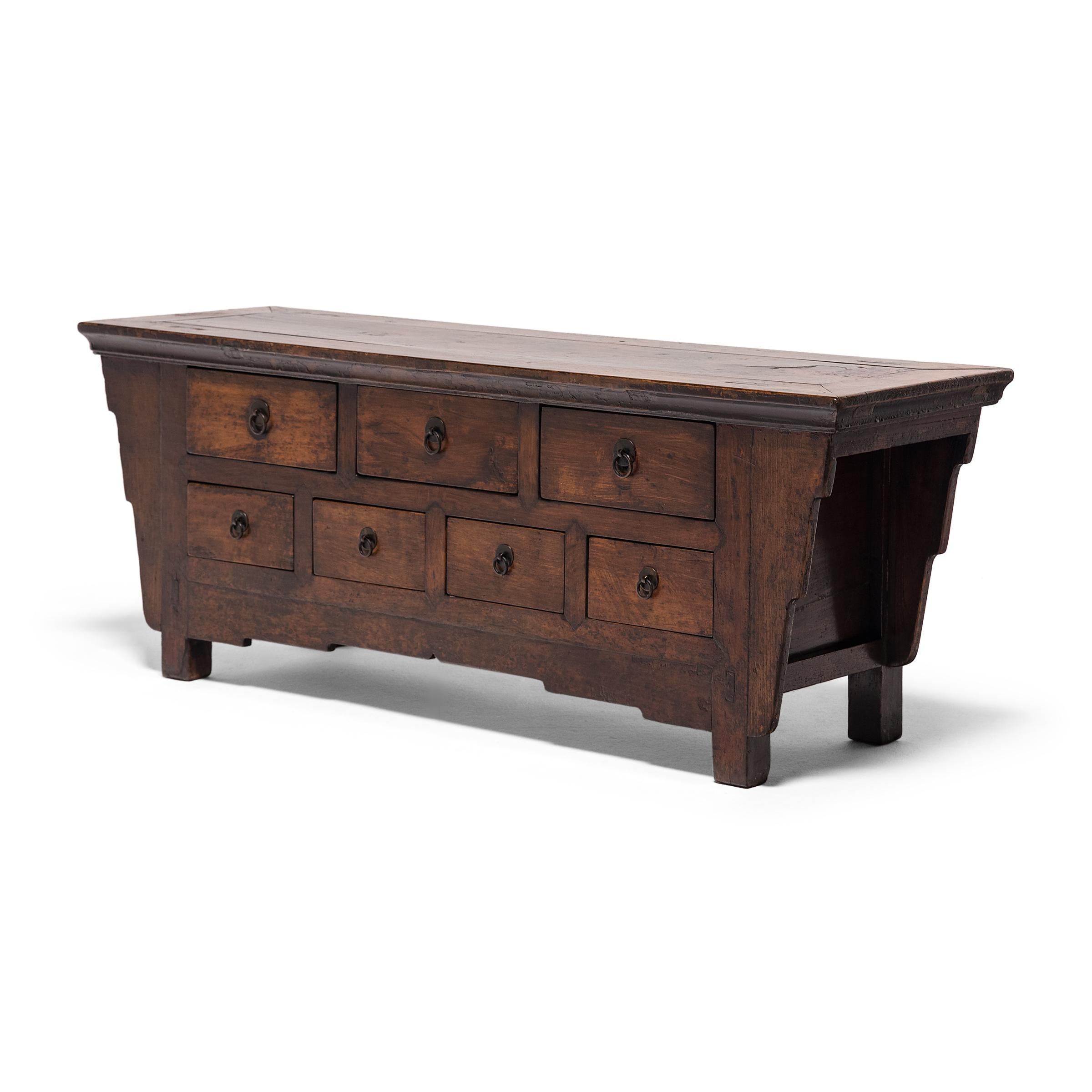 This low seven-drawer chest dates to the late 19th century and is crafted of northern elm (yumu) using traditional mortise-and-tenon joinery methods. The low cabinet features seven drawers enclosed by a stepped apron and an expansive floating-panel