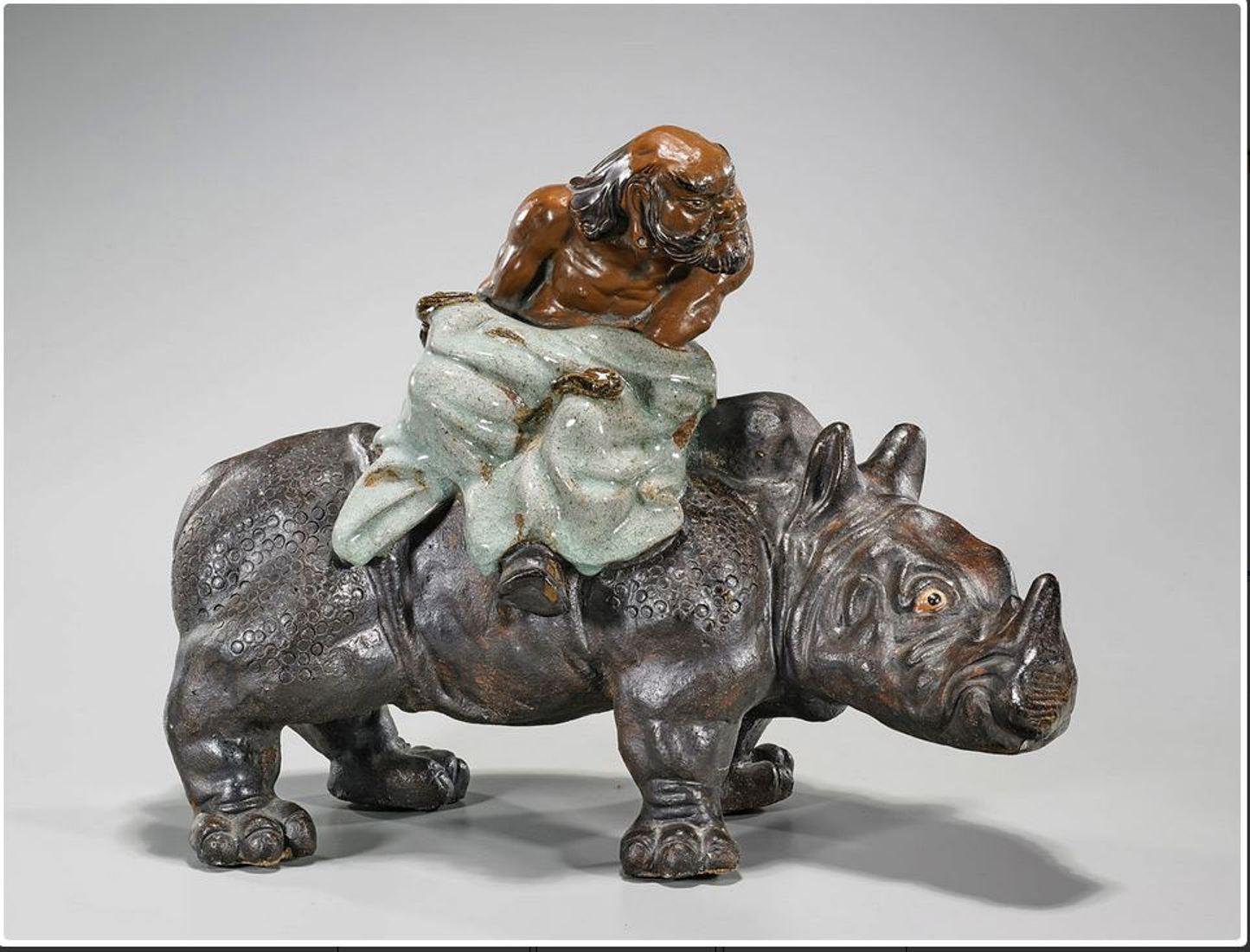 A very decorative Chinese Shekwan glazed pottery figural sculpture of a seated Lohan riding a rhinoceros.