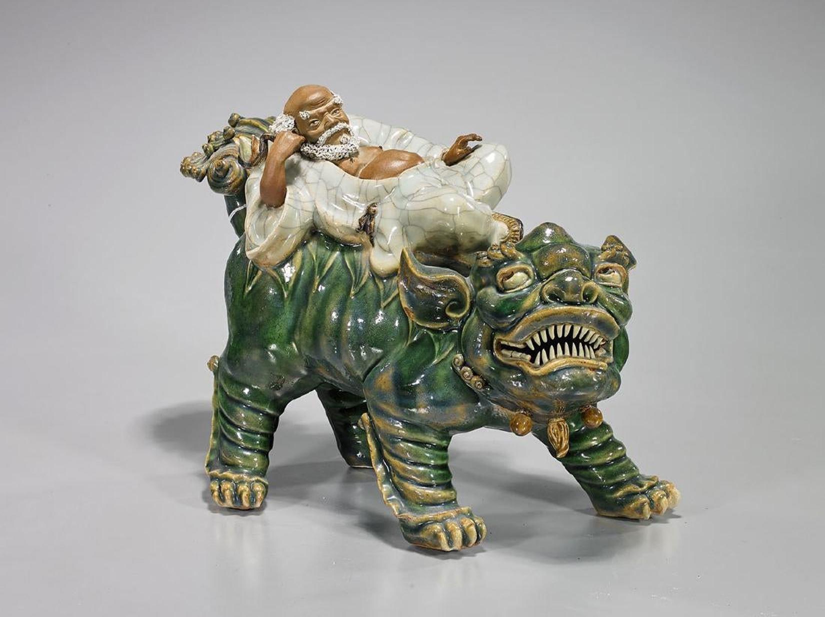 A highly decorative Chinese Shekwan glazed pottery sculpture of a reclining Lohan over a green glazed fulion.
Late 20th century (possibly earlier).
 
