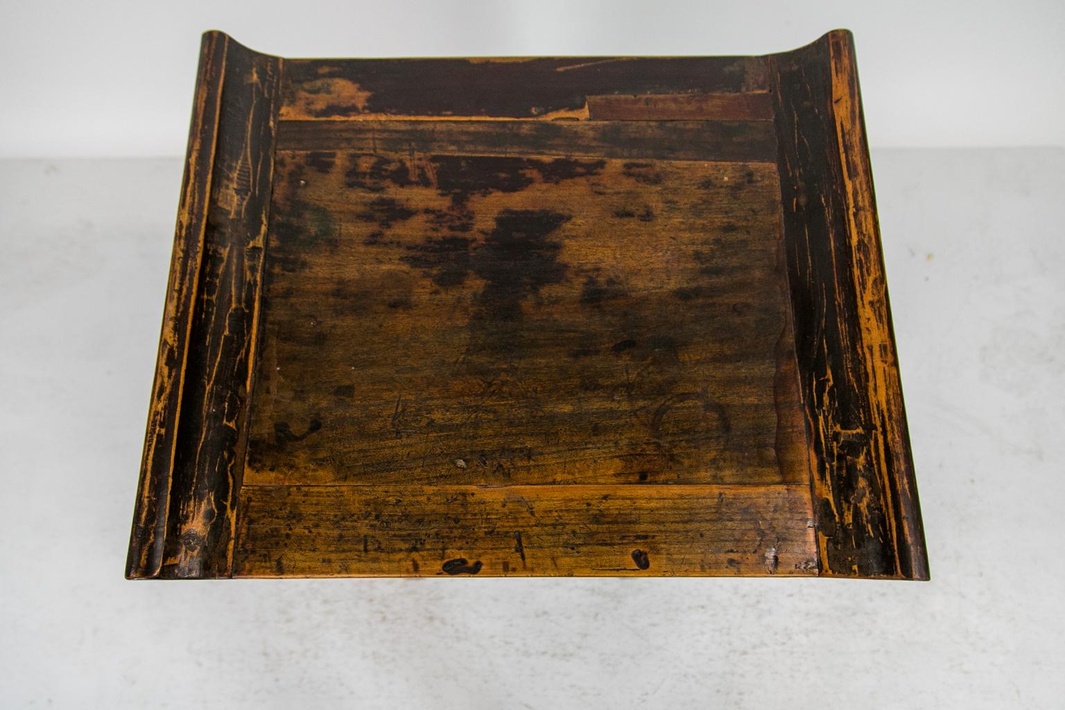 This Chinese side table has carved floral openwork supporting side wings and a lower apron. It has its original stylized butterfly brass drawer pull framed by a carved arch.
  