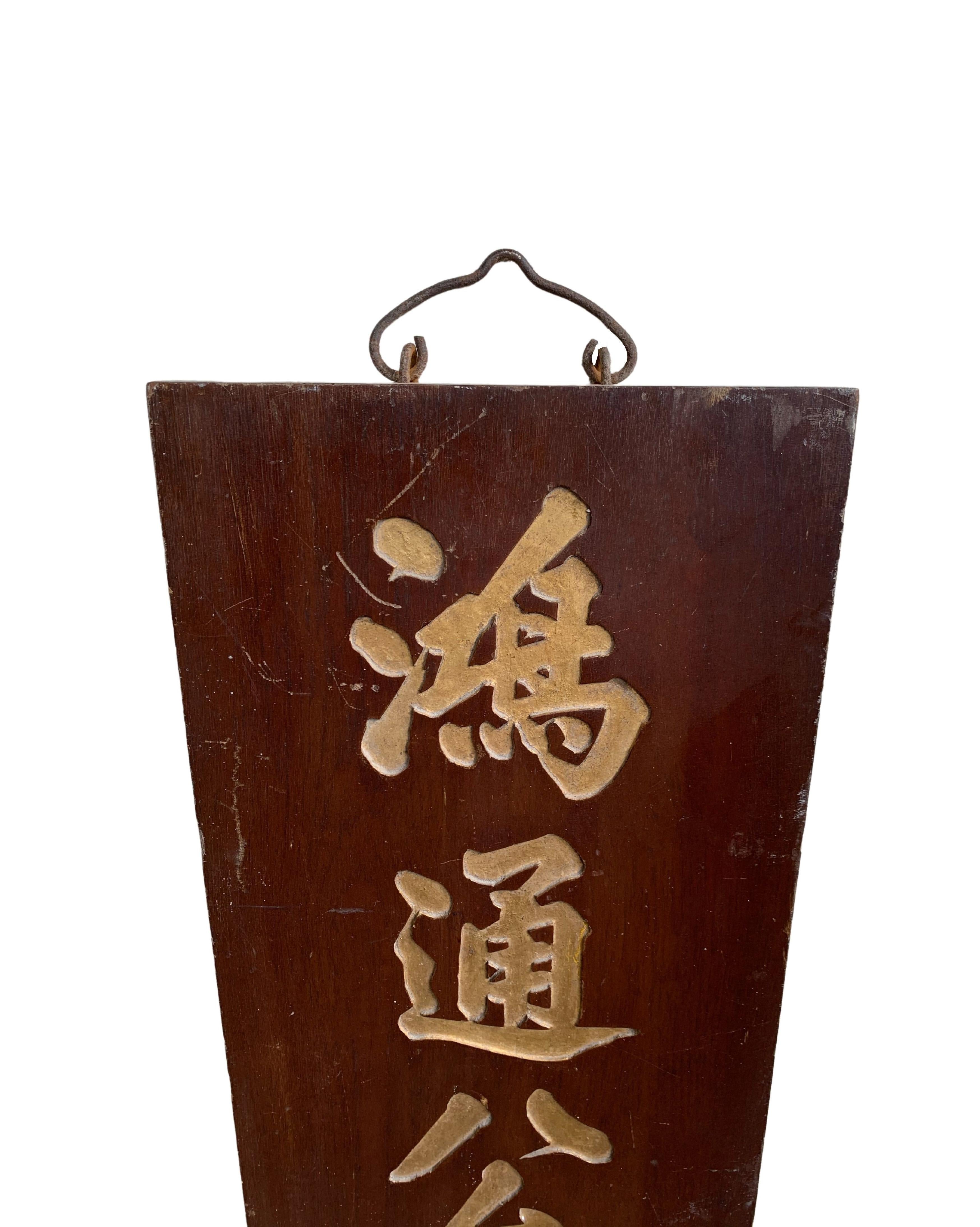 Mit einem holzfarbenen Sockel hebt dieses Schild (das komplett aus Holz gefertigt ist) 3 große goldfarbene chinesische Schriftzeichen hervor. Das Schild stammt aus der Mitte des 20. Jahrhunderts und ist durch die Alterung des Holzes und das