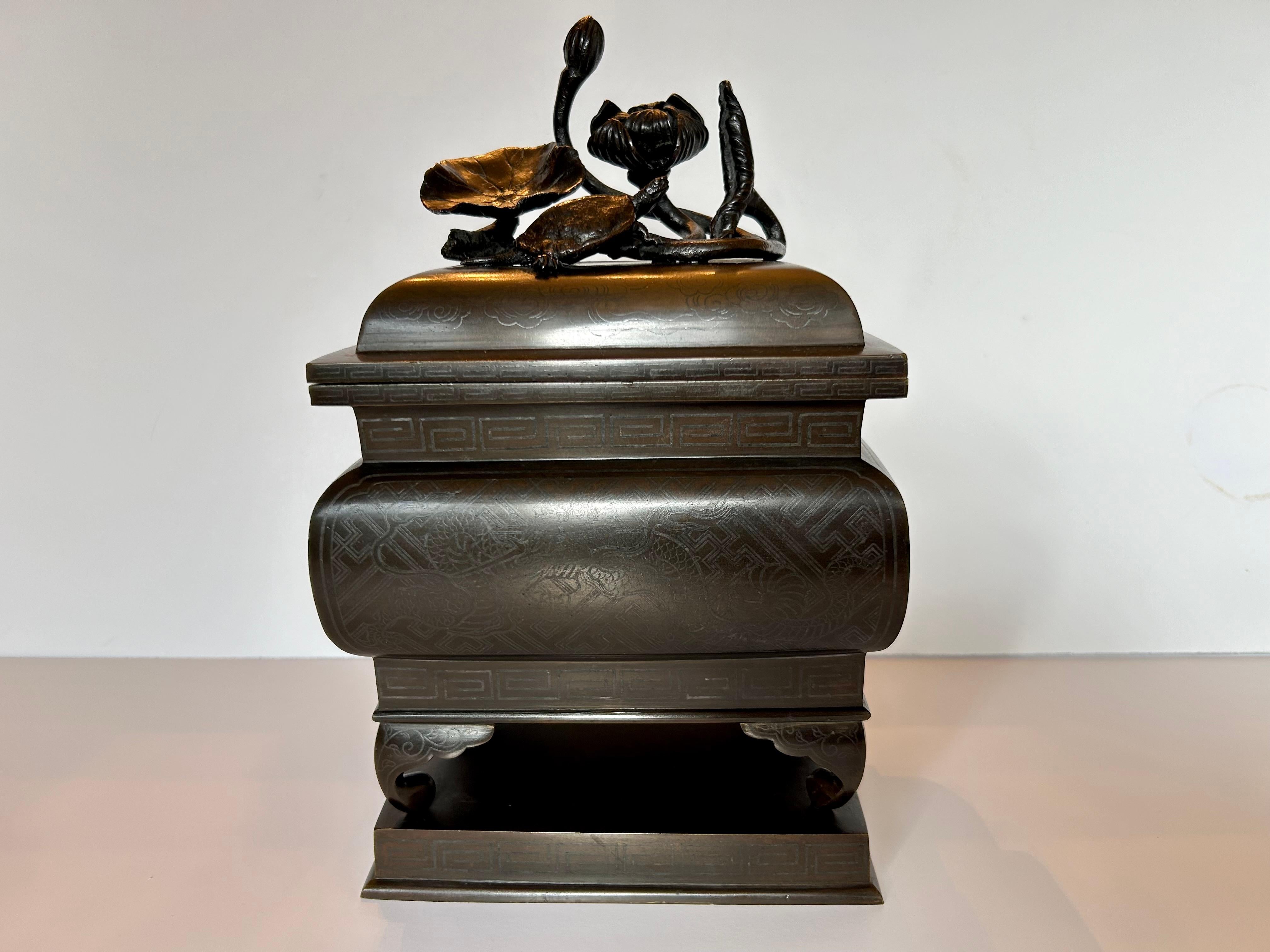This is a wonderful Japanese,  silver inlaid, solid Bronze incense burner from the late 19th century or early 20th century.
The removable lid features beautiful modelling of a small turtle climbing over lily pads whose flowers are about to burst
