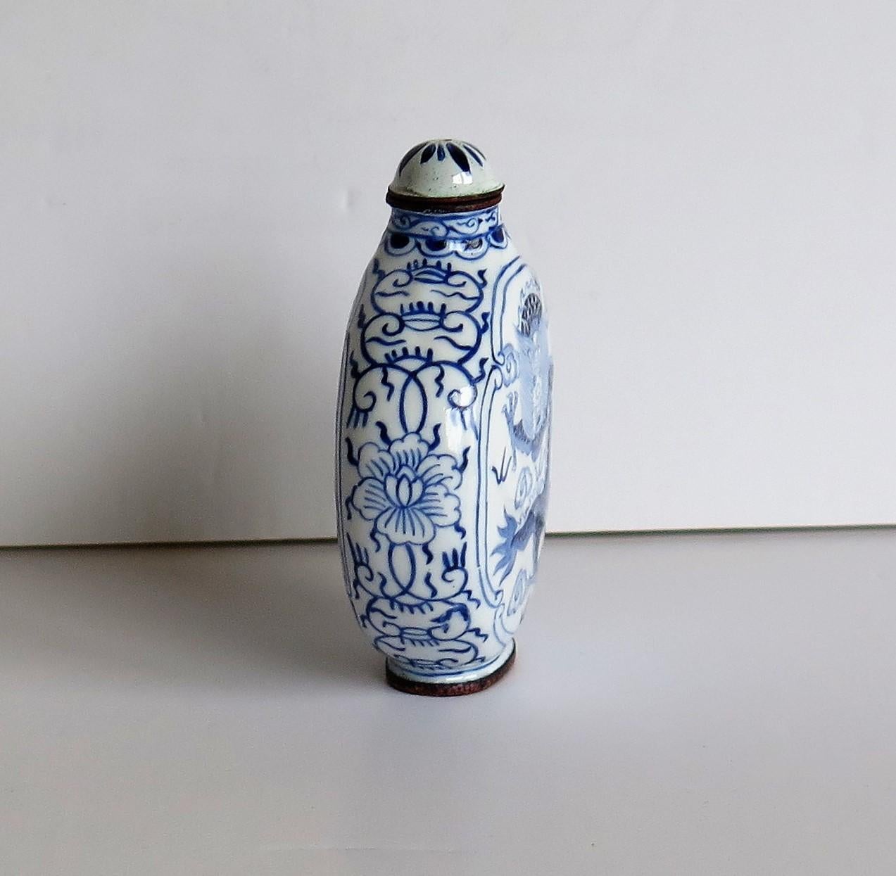 This is a Chinese enamelled snuff bottle, with a hand painted blue and white dragon on either side and a four character mark to the base, which we date to the 1940s.

The circular body of this bottle is made of copper or bronze. There is a hand