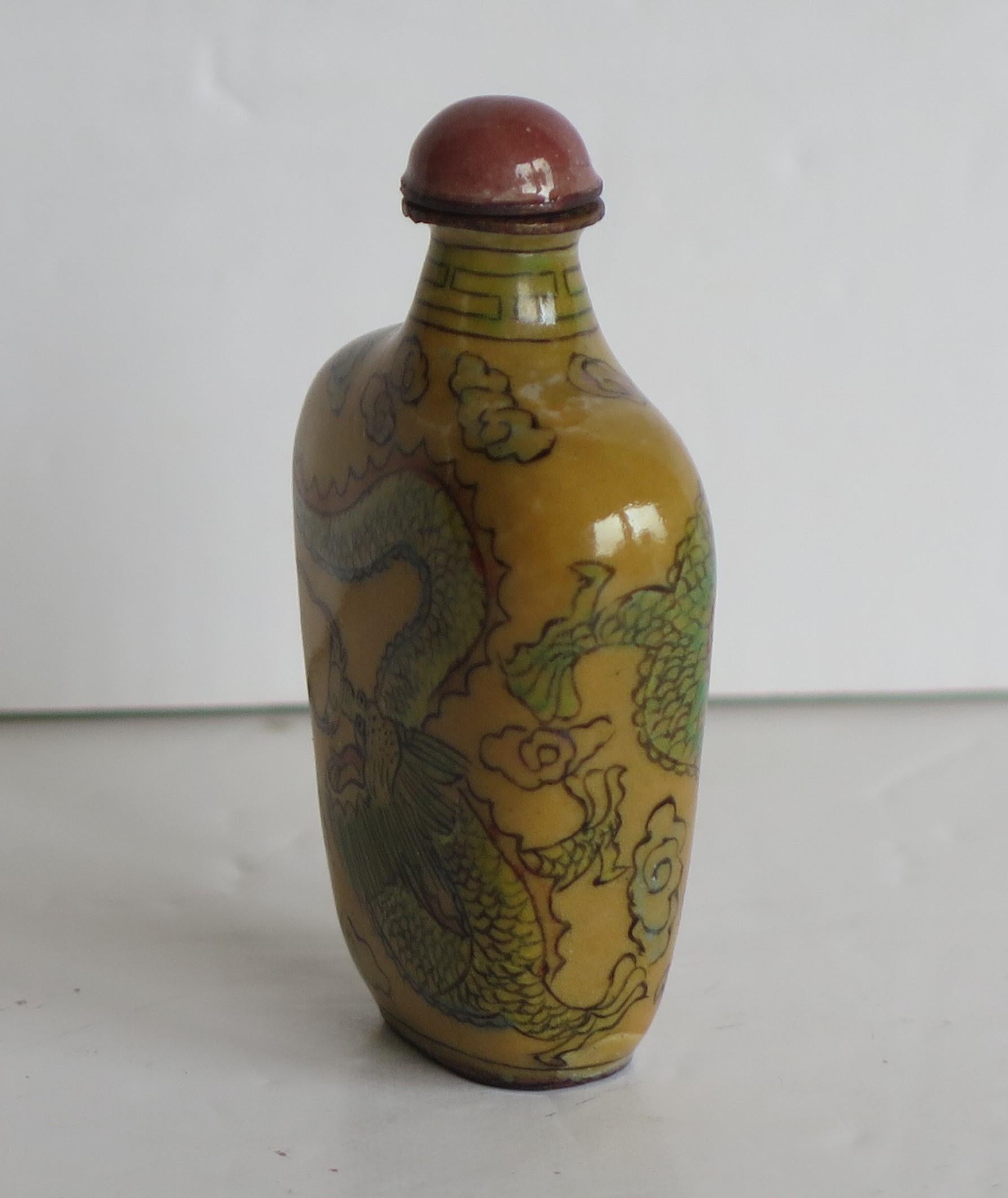 This is a Chinese enamelled snuff bottle, with two hand painted dragons chasing a flaming pearl, with a neck border pattern, together with a spoon top, which we date to the 1920s.

The rectangular section tapering body of this bottle is made of