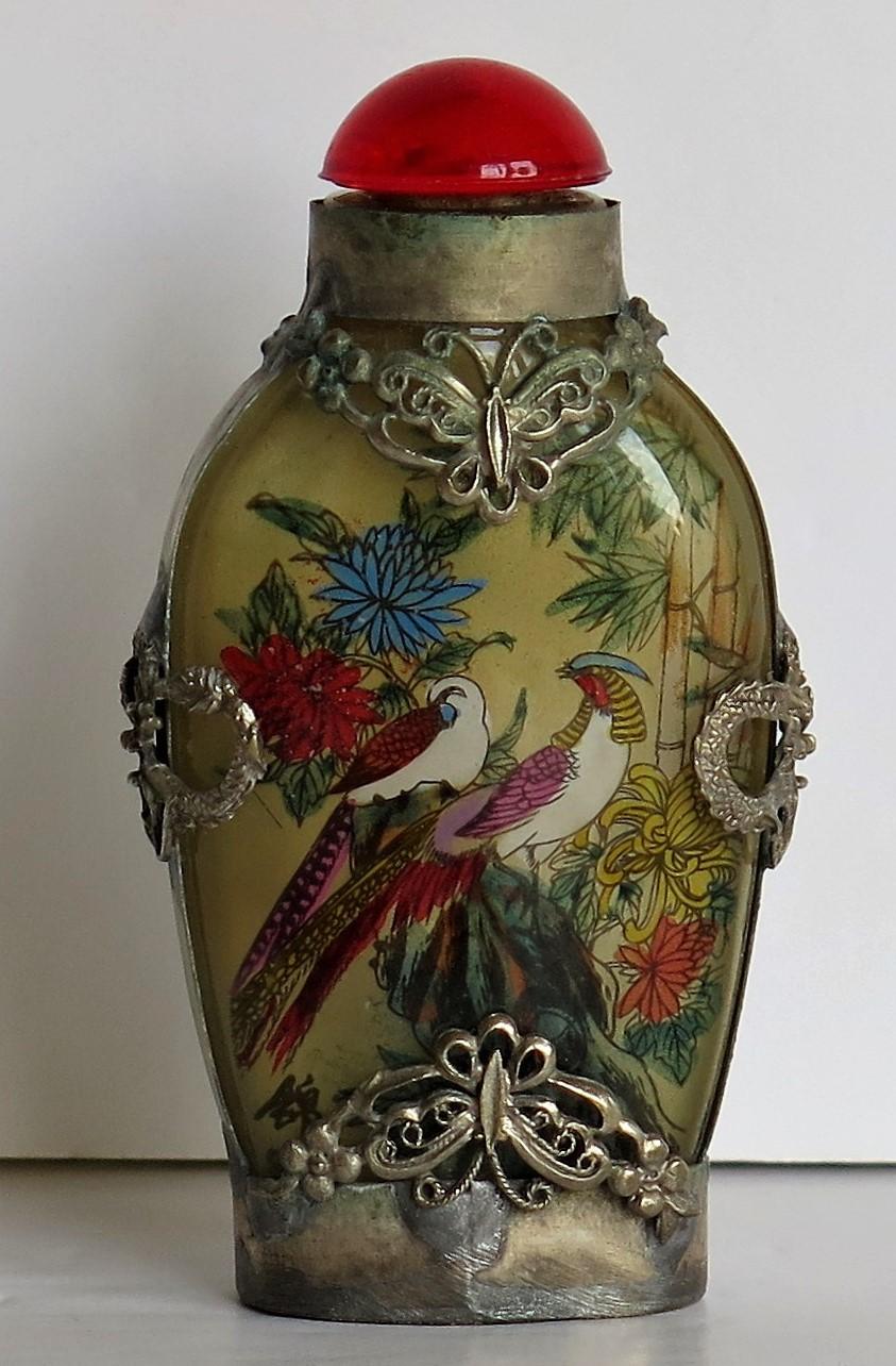 This is a very good Chinese glass snuff bottle with a Miao Silver case, the bottle being beautifully inside hand painted and dating to the mid-20th century, circa 1940.

It is made of a smooth glass which has then been very finely hand painted to
