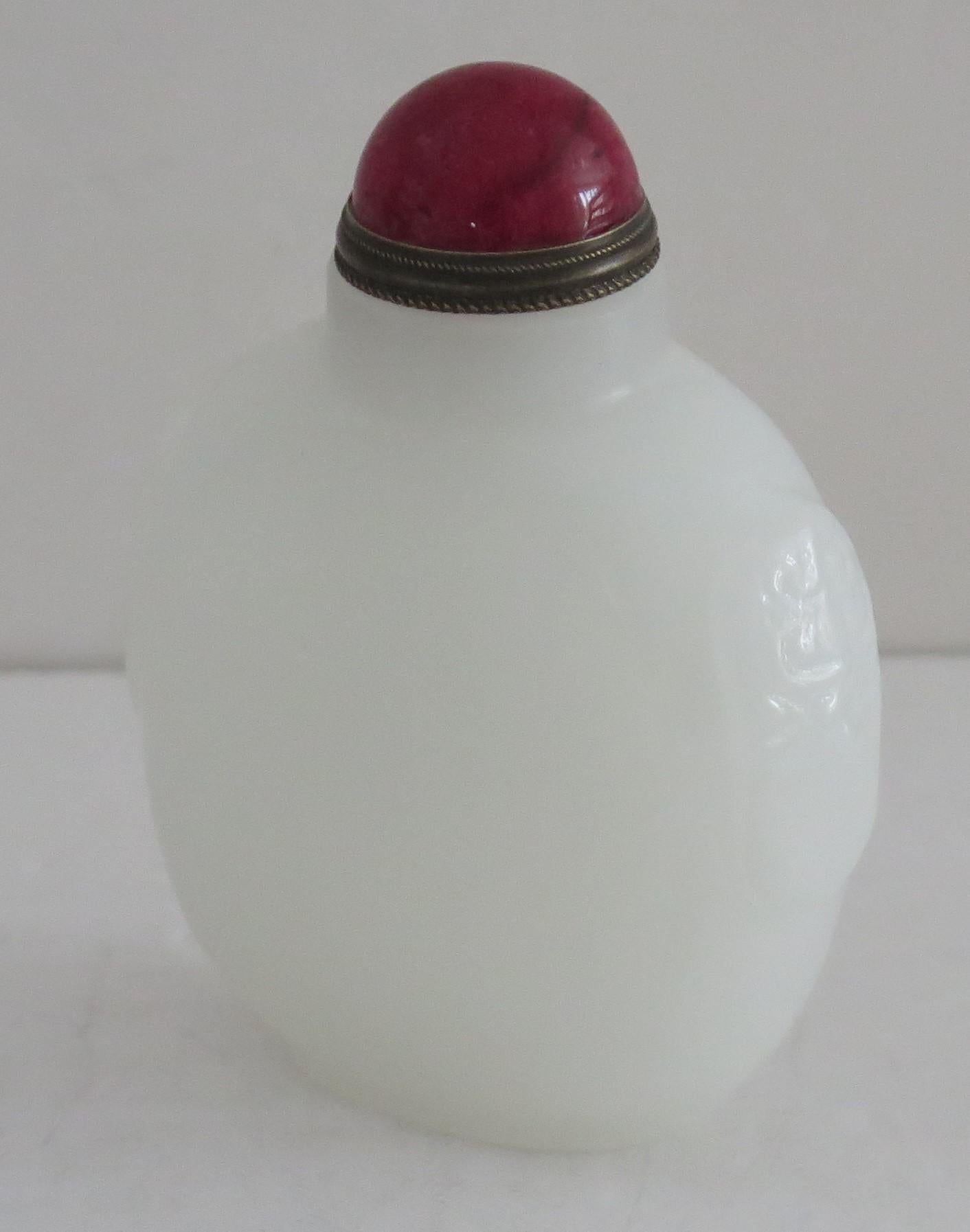 This is a beautiful Chinese snuff bottle, made of a white stone with a red stone top and spoon, dating to the mid 20th century.

The bottle is hand carved and polished from a type of stone having a lovely milky white colour with hand-carved detail