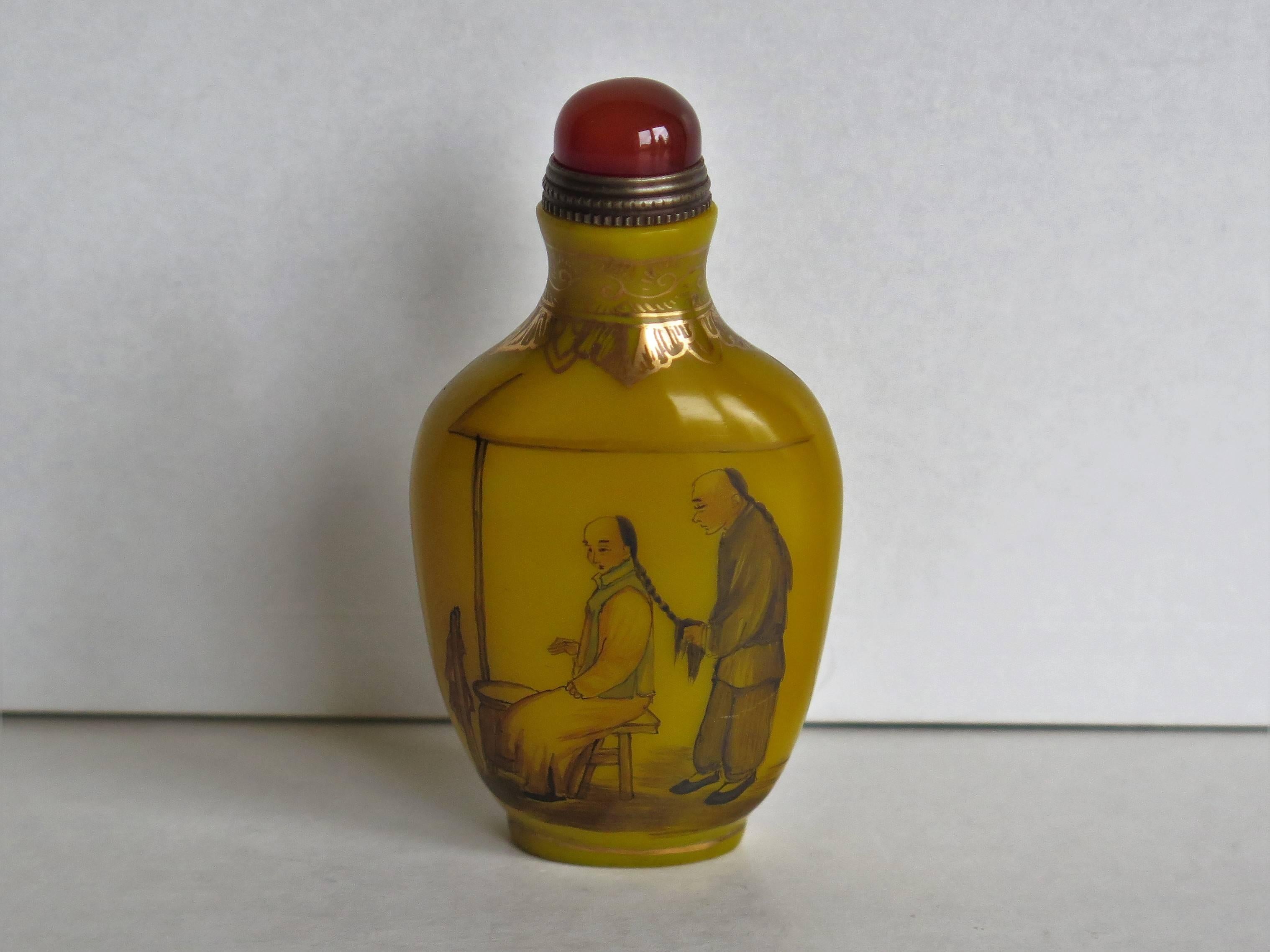 This is a very good Chinese snuff bottle, which we date to the earlier part of the 20th century, circa 1920

It is made of a yellow milk glass which has then been hand-painted in colored enamels with scenes of 18th century Chinese people, with a