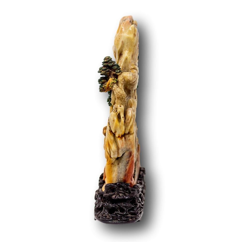 Chinese soapstone carving of exceptional quality upon a hardwood base. The carving featuring a mountain with green foliage throughout with a central depiction of a Deity and Child bearing a rucksack below a staircase up the mountain. The soapstone