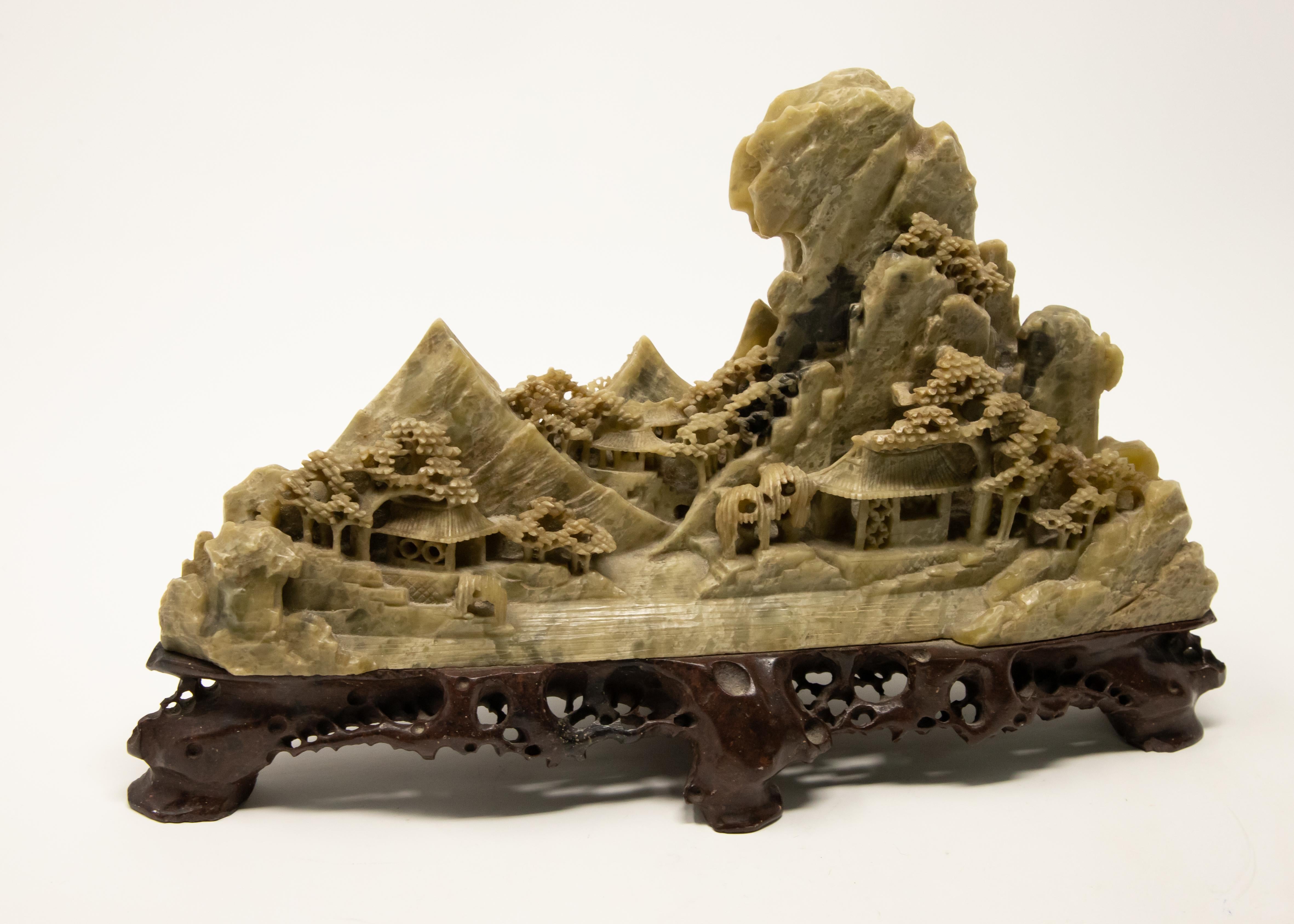 Offering this stunning soapstone carving of a Chinese landscape. The base is a carved piece of wood with openwork detail. The soapstone is mounted to the wood and starts at the base with two shelters, trees and rocks. In the background is mountains