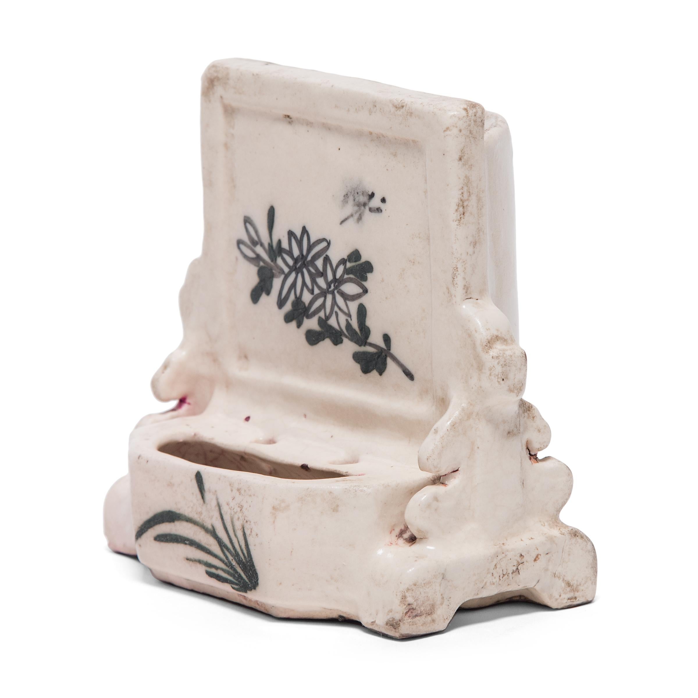 Set beside the four treasures of the scholars' studio, brush washers were used by Qing-dynasty scholars to rinse ink from calligraphy brushes. This porcelain brush washer is sculpted in the shape of a spirit screen painted with flowers and tall