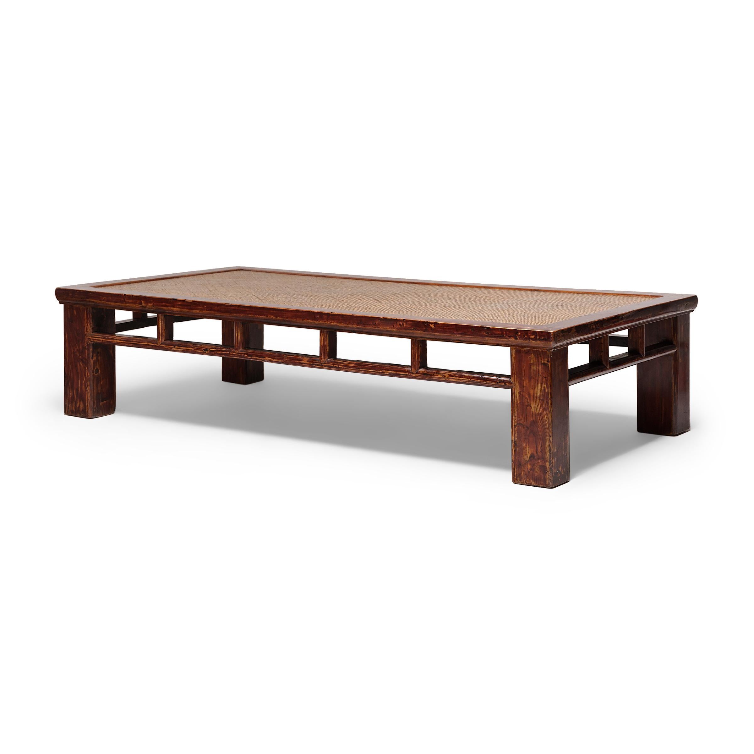 Dated to the early 20th century, this low daybed has a timeless simplicity, featuring a woven rattan top, four square legs and an open, clean-lined apron. The frame is crafted of northern elm (yumu) using mortise-and-tenon joinery and finished with