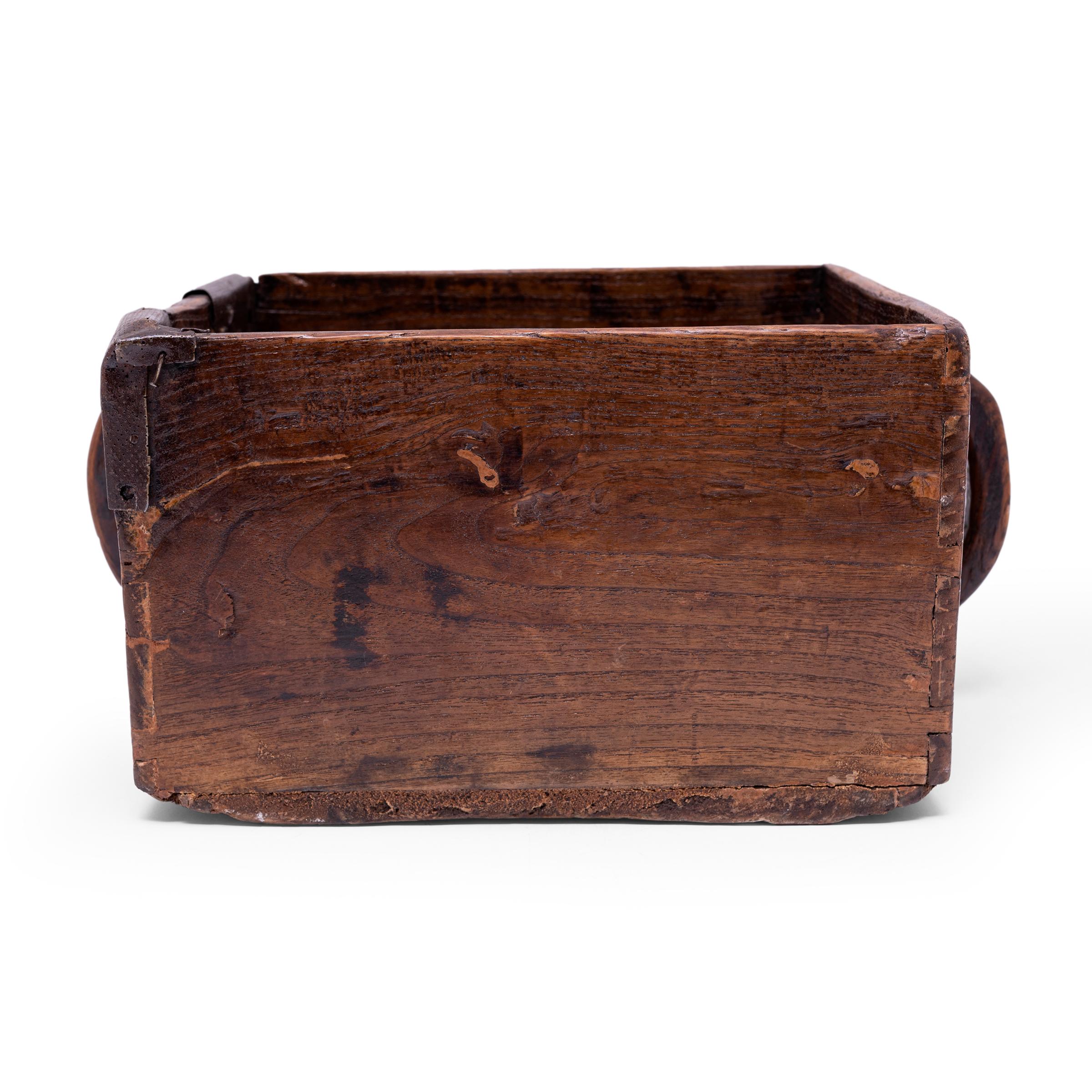 This rustic container was made over a hundred years ago to measure and hold a dou of rice, an ancient Chinese measurement. The wooden box is hand-crafted with a square body, straight sides, and two arched side handles. Antique iron repairs reinforce