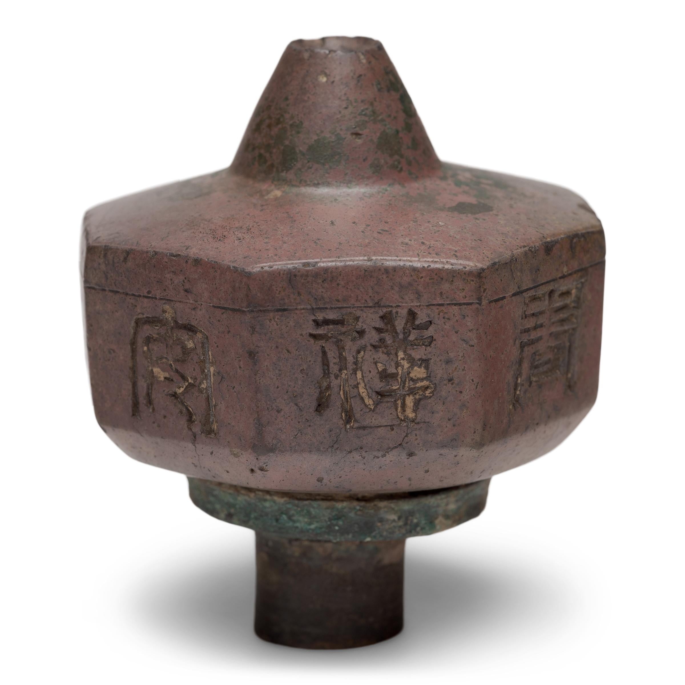 Cet objet inhabituel est un fourneau de pipe à opium du XIXe siècle, sculpté dans de l'argile foncée pour obtenir une forme à huit côtés, avec un embout conique et un collier en laiton. Minimal et raffiné, le fourneau de la pipe est décoré de grands