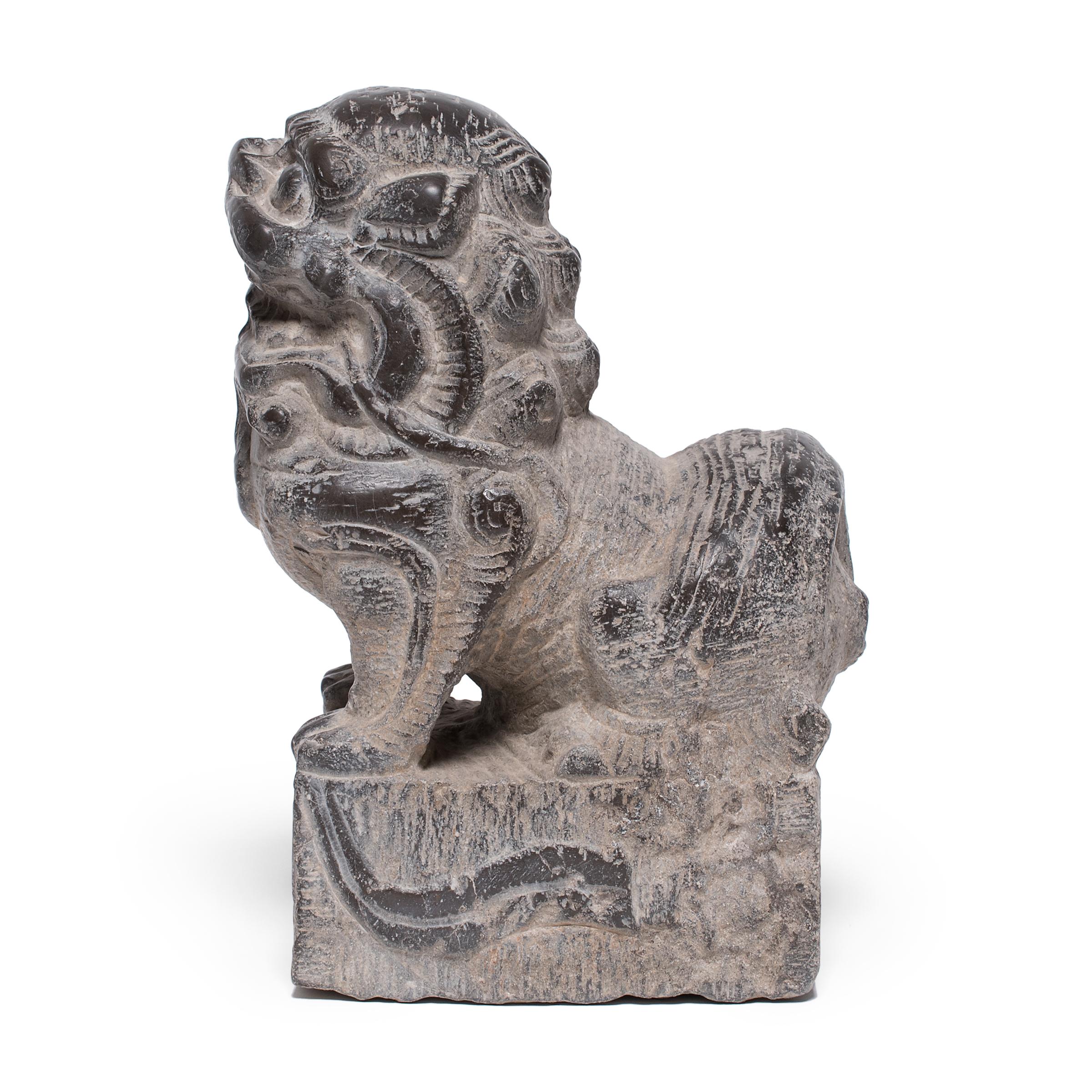 Hand-carved from a single block of limestone, this stone fu dog sits at attention as a watchful guardian of the home. He exudes a remarkable sense of life and energy - crouched on all fours with curly hair and a lively expression. A bell hanging