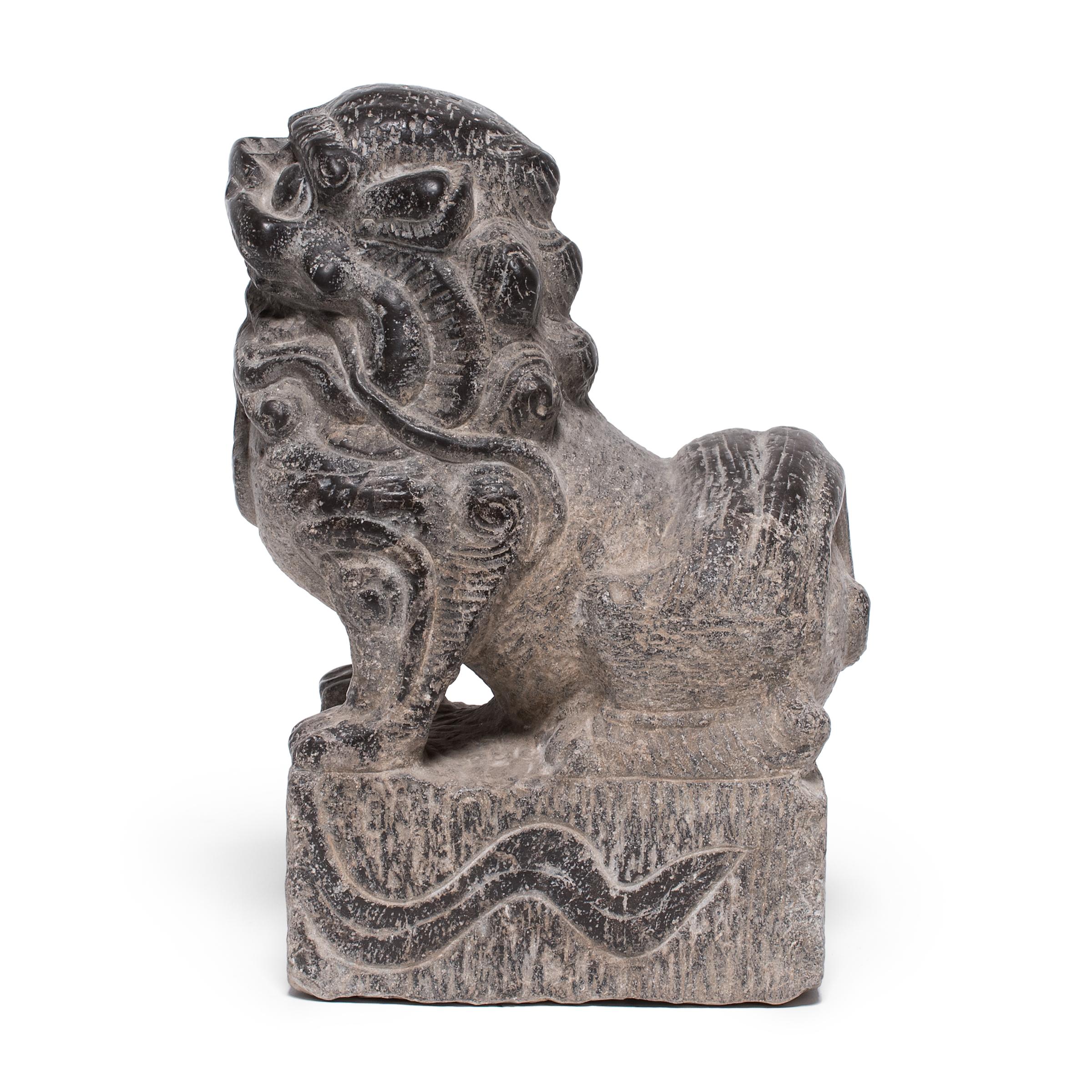 Hand-carved from a single block of limestone, this stone fu dog sits at attention as a watchful guardian of the home. He exudes a remarkable sense of life and energy - crouched on all fours with curly hair and a lively expression. A bell hanging