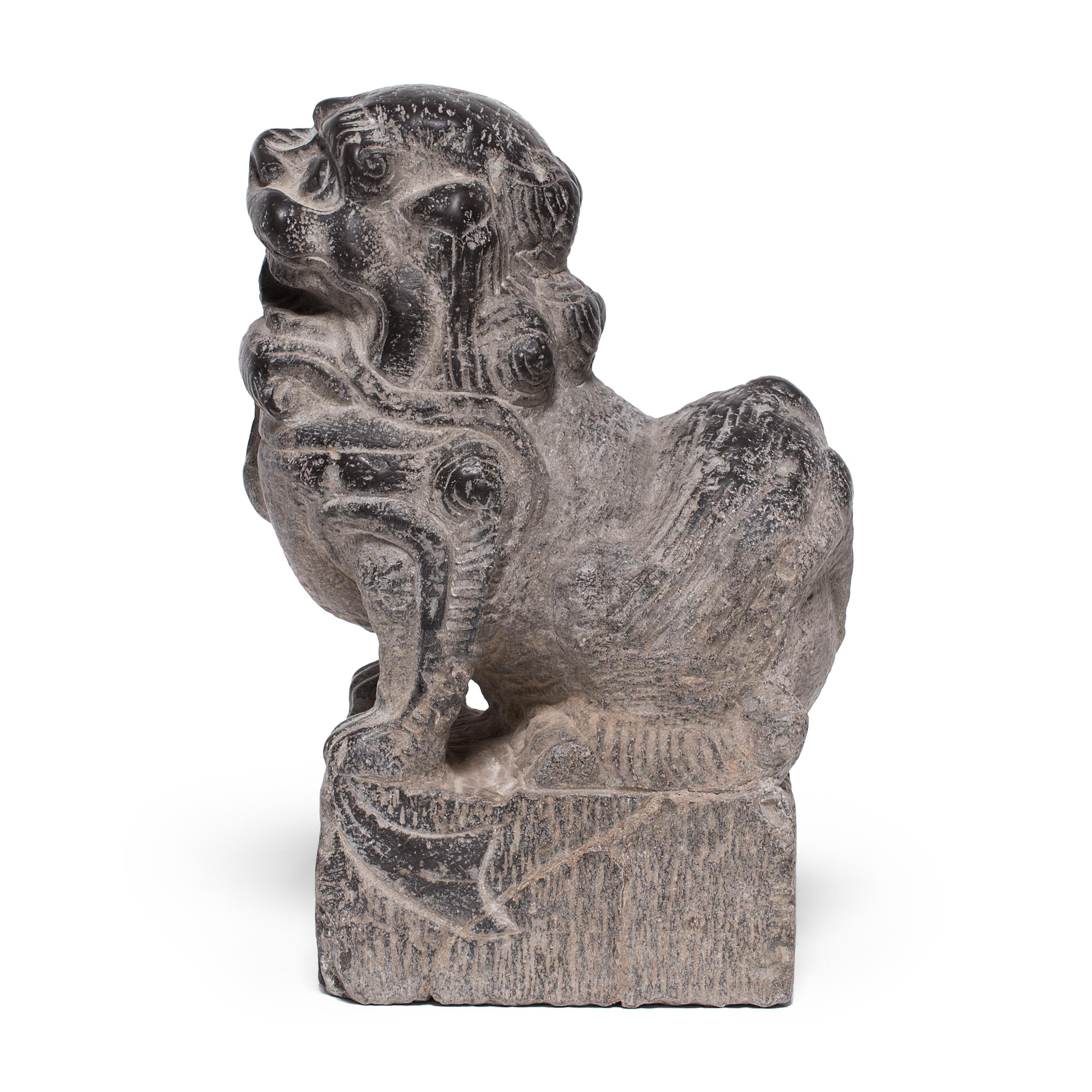 Hand-carved from a single block of limestone, this stone fu dog sits at attention as a watchful guardian of the home. He exudes a remarkable sense of life and energy - crouched on all fours with curly hair and a lively expression. A bell hanging