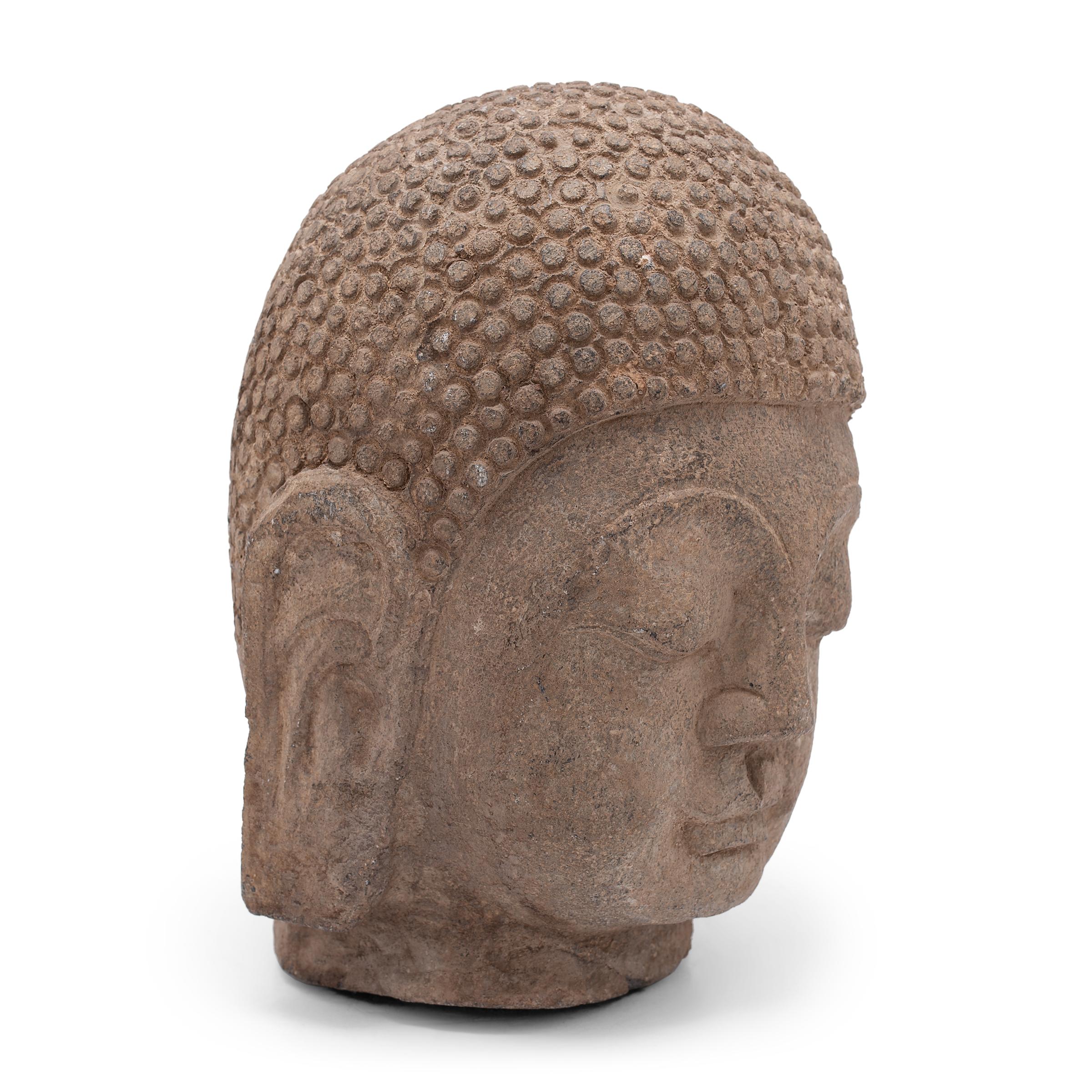 With closed eyes and a gentle expression, this large stone Buddha head brings calm and serenity to its surroundings. The hand-carved figure depicts the historic Buddha Shakyamuni, also known as Shaka, Gautama Buddha, or Prince Siddhartha. Commonly