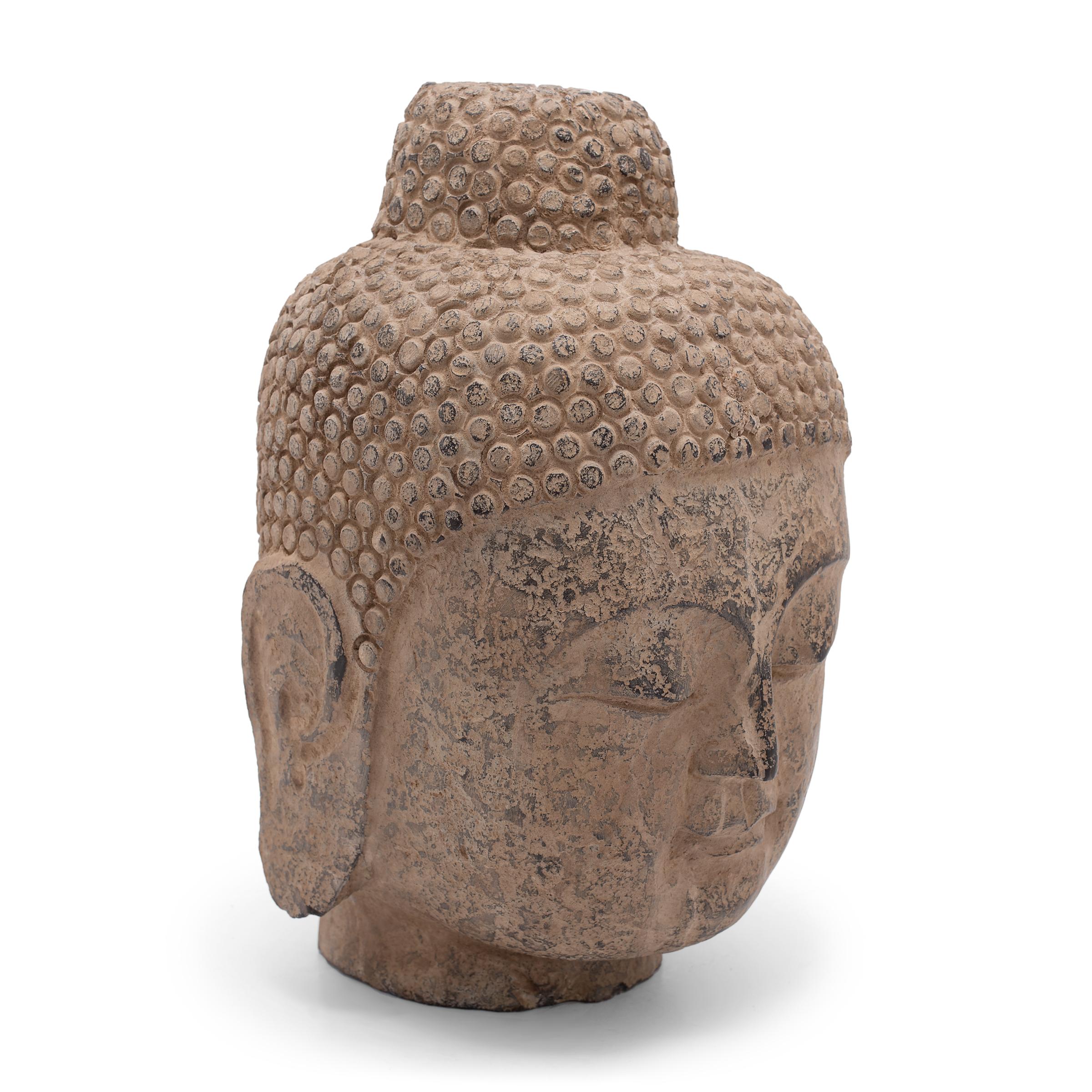With closed eyes and a gentle expression, this large stone Buddha head brings calm and serenity to its surroundings. The hand-carved figure depicts the historic Buddha Shakyamuni, also known as Shaka, Gautama Buddha, or Prince Siddhartha. Commonly