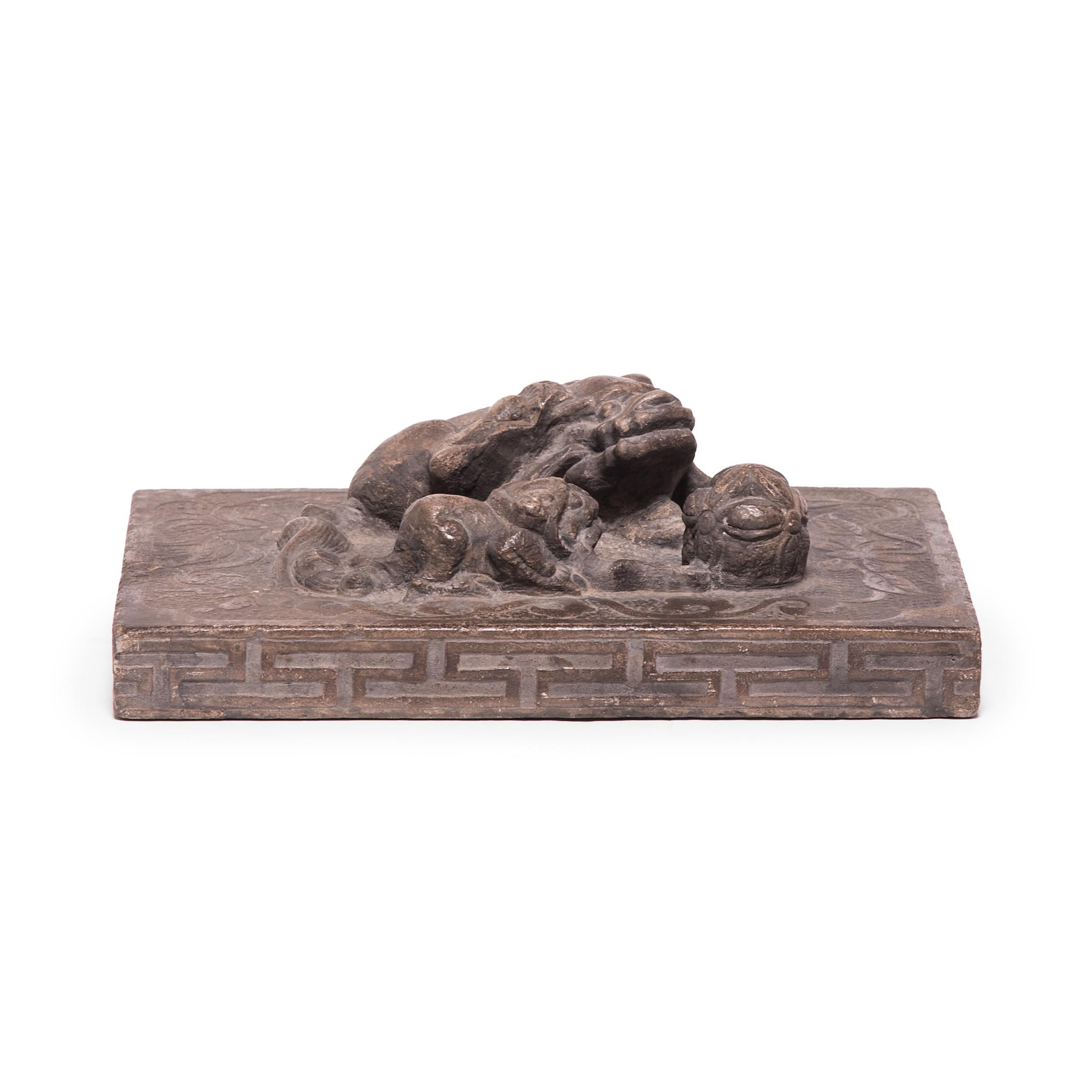 Carved from a solid piece of stone, this weight was originally used by a Shoemaker to press down large pieces of leather. Surrounded by intricate scrollwork and peony blossoms, a guardian fu dog lies beside her cub, each biting the thread of an