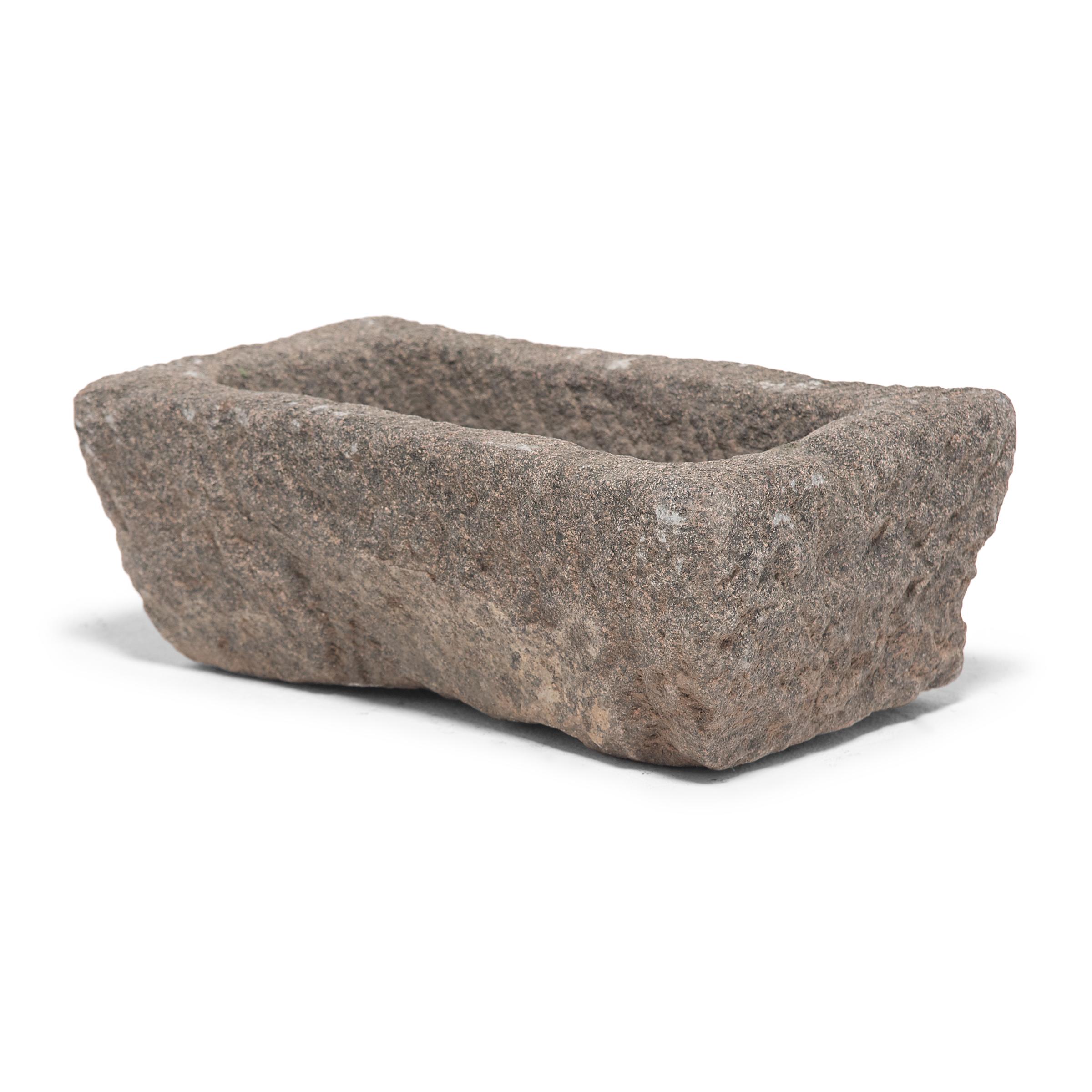 Once a common sight in courtyards throughout rural China, this textured stone vessel was used as a grain trough for chickens and other barnyard fowl. Chiseled from a block of granite over a century ago, the sculptural trough charms with its uneven